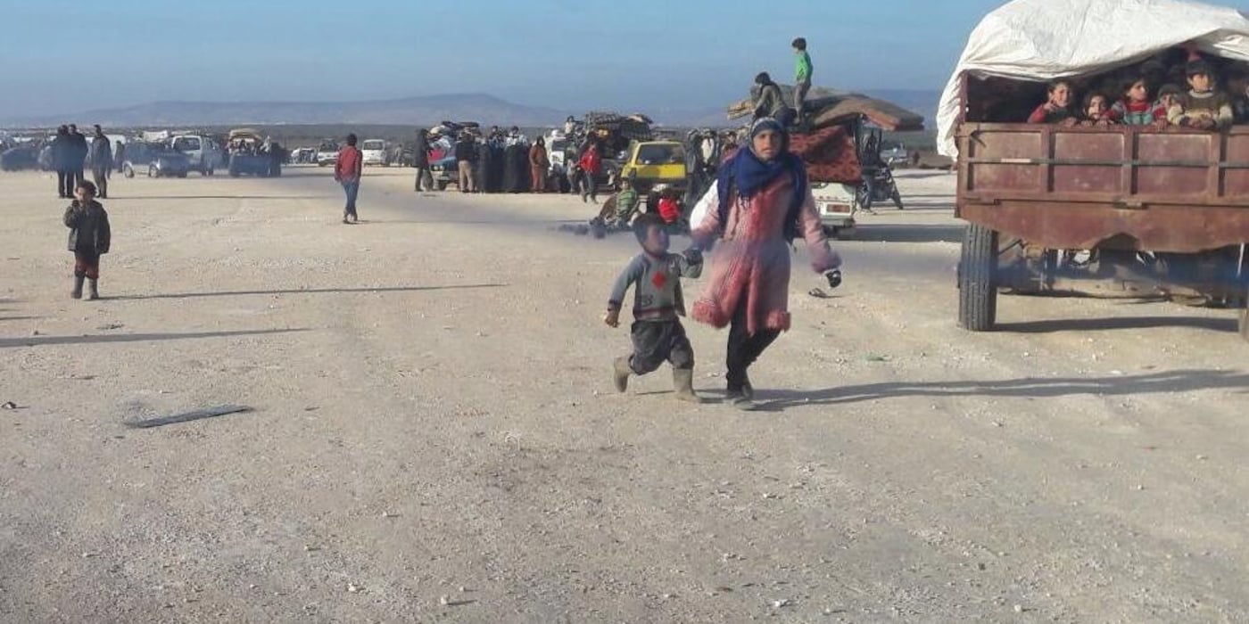 Recently displaced Syrian families walking towards the Bab Al Salama border crossing gates with all they can carry. Thousands of people have gathered at the border hoping and praying they could be let through. According to sources, families were told the border gates would not be opened and to leave the area. We notice in the photo a small child looking lost, holding the hand of a police man. Family separation is not uncommon during such times of chaos. Photo: NRC