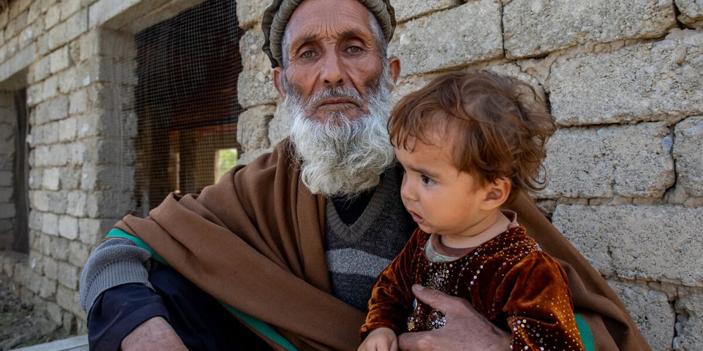 En äldre man håller ett litet barn utanför sitt hem i Afghanistan.