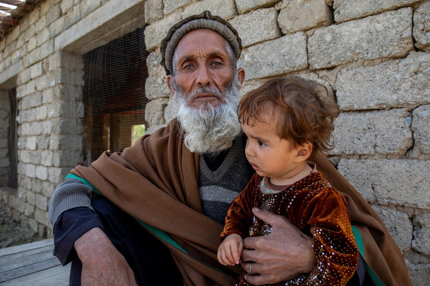 En äldre man håller ett litet barn utanför sitt hem i Afghanistan.
