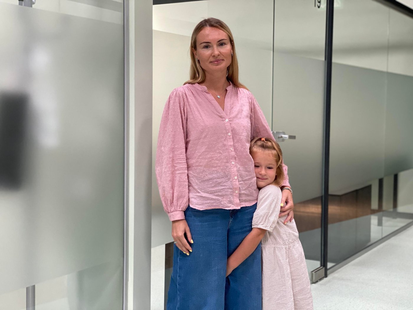 A mother and daughter both dressed in pink standing in front of a grey wall.