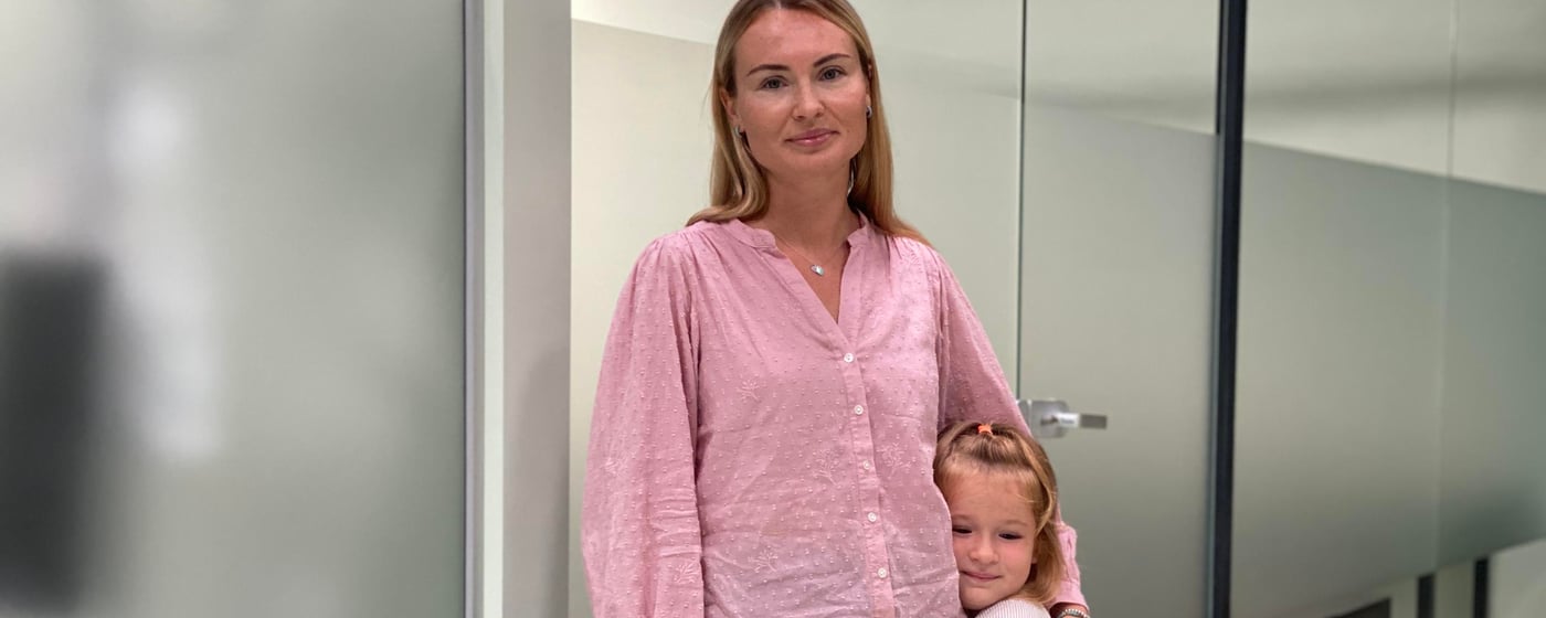 A mother and daughter both dressed in pink standing in front of a grey wall.