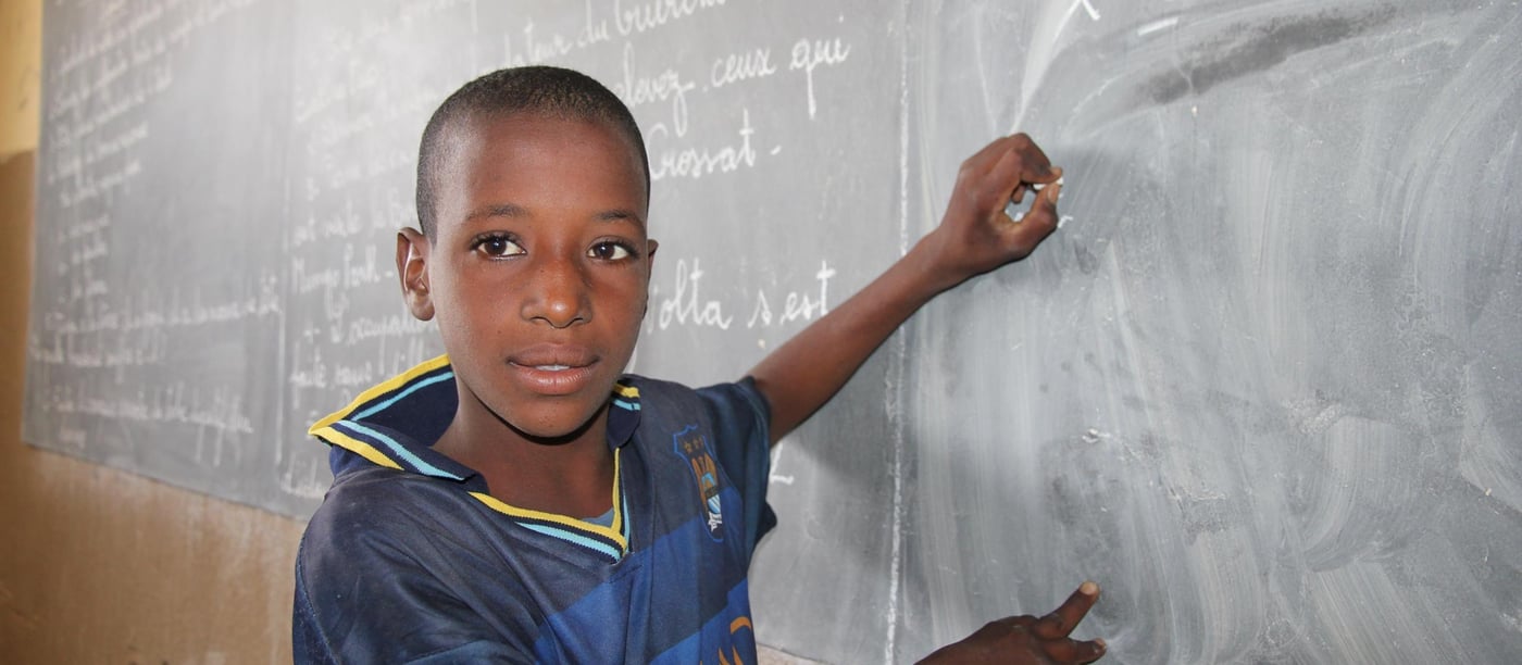 Ali 15 year old (boy in blue shirt with stripes) is writing on the black board in the classroom. He loves school, and geography is his favorite subject. Ali wants to join the armed forces when he grows up.

Education:

NRC has through the years provided different types of education programs. In 2013-2015 NRC ran an education project in the Mentao refugee camp comprising a catch-up programme for children of school going age who have been forced to drop out of school. NRC also had  a YEP program (combining literacy educational and learning crafts) for youths between the ages of 15 to 24 who can no longer make in into the normal school system. 163 pupils completed the catch-up programme while 105 youths completed the YEP programme   

Now NRC is providing education for smaller children in the Goudebo camp; Ecole Primaire de Goudebo has between 800 and 900 pupils aged from 6 to 12 years, divided in six grades. The number of pupils differs with families trying to return to their country of origin. Return programme is facilitated by UNHCR.

Most of the pupils are refugees, but the school also has some pupils from the host community.

There are 6 grades at the school. In the first two years (CP 1 and CP 2), there are two teachers in each class. Because the school language is French, and many of the refugee children do only speak local Tuareg dialects, they need help for translation to be able to follow the education. (Official schools in Mali is also teaching in French)

NRC target that 50% of all pupils should be girls is met in the vast majority of the classrooms. The age of the children in each class differs. Most of the children arriving in the camp have never gone to school before, so they have to start in the basic class regardless of their age. 

Most of the pupils have books to write in, but in a few classes the pupils still uses small wooden boards and chalk. 

Photo: NRC/Ingrid Prestetun