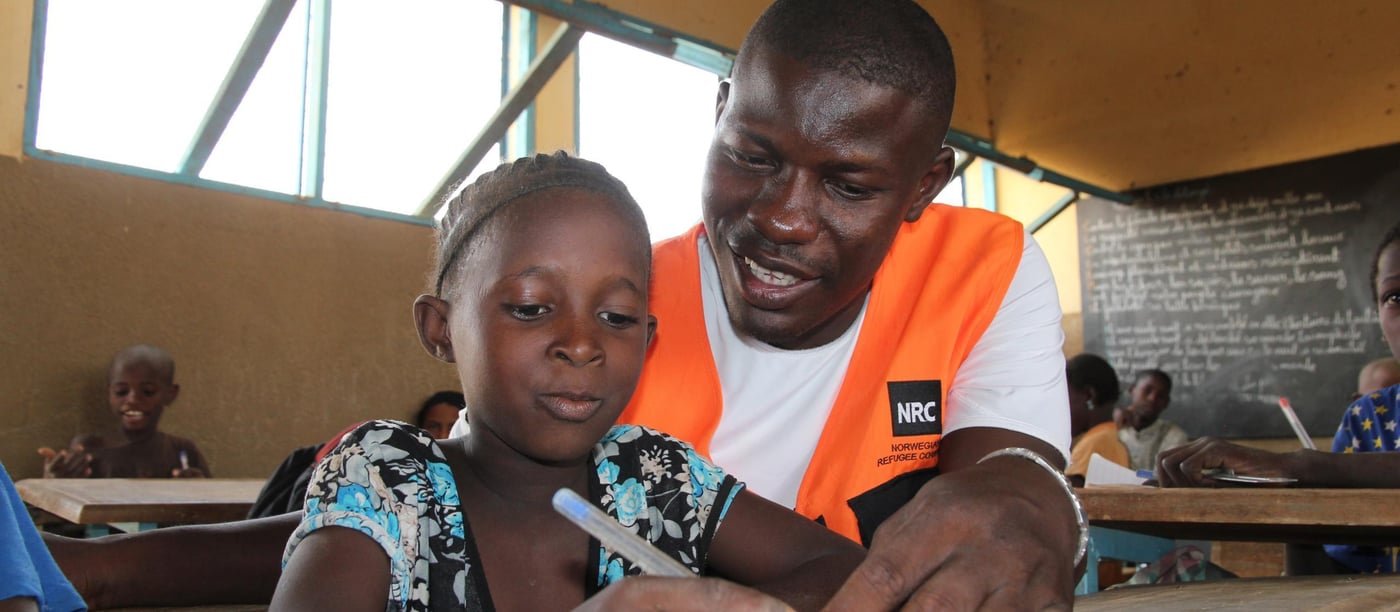 Aminatou (8 years) (blue/grey/black flowered dress) together with NRC education officer Adama Kougoro in the classroom at the school in Goudebo refugee camp.  She likes reading very much and wants to be a teacher when she grows up. 

NRC has through the years provided different types of education programs. In 2013-2015 NRC ran an education project in the Mentao refugee camp comprising a catch-up programme for children of school going age who have been forced to drop out of school. NRC also had  a YEP program (combining literacy educational and learning crafts) for youths between the ages of 15 to 24 who can no longer make in into the normal school system. 163 pupils completed the catch-up programme while 105 youths completed the YEP programme   

Now NRC is providing education for smaller children in the Goudebo camp; Ecole Primaire de Goudebo has between 800 and 900 pupils aged from 6 to 12 years, divided in six grades. The number of pupils differs with families trying to return to their country of origin. Return programme is facilitated by UNHCR.

Most of the pupils are refugees, but the school also has some pupils from the host community.

There are 6 grades at the school. In the first two years (CP 1 and CP 2), there are two teachers in each class. Because the school language is French, and many of the refugee children do only speak local Tuareg dialects, they need help for translation to be able to follow the education. (Official schools in Mali is also teaching in French)

NRC target that 50% of all pupils should be girls is met in the vast majority of the classrooms. The age of the children in each class differs. Most of the children arriving in the camp have never gone to school before, so they have to start in the basic class regardless of their age. 

Most of the pupils have books to write in, but in a few classes the pupils still uses small wooden boards and chalk.

Photo: NRC/Ingrid Prestetun