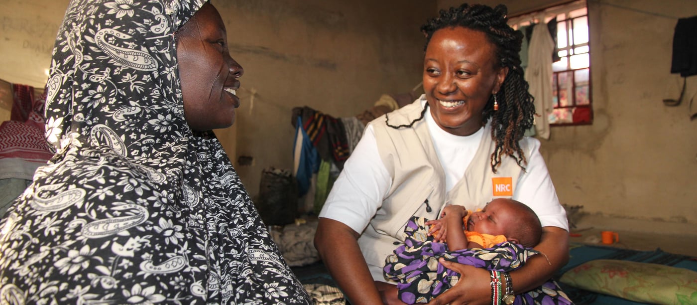 While on a house visit to some of the displaced families living in Bakasi camp NRC Nigeria’s Country Director Maria Wangechi warmly holding Aisha’s baby Ya’Ya`fanna together with Aisha, both happily conversing with each other. 

Aisha is a 30 year old mother of five.  Her last born child is Ya´fanna, who is one month old.  Ya´fanna was born in the Bakasi displaced persons camp that is located in the outskirts of Maiduguri, a bustling city that is the capital of Borno state in North East Nigeria. Aisha together with her husband and children have been living in their one room space at the camp since 2015 when they had to flee from their home.
Aisha’s husband Alhaji is 46 years old.  He used to be a livestock trader in their hometown of Guzamala which is close to 90 km away from Maiduguri.  On one Sunday afternoon, the neighbouring town of Mangano was attacked by the insurgents and the rumours of an impending attack on their village quickly reached Aisha and her family.  Her husband made the quick decision to move his family from the area, fearing for his then pregnant wife and young children.
They left immediately and did not have time to carry any of their belongings.  The only possession they had was her husband’s motorcycle that was soon became cumbersome due to the dessert terrain.  They soon abandoned the motorcycle and travelled by foot for about 40 km to Ngenzai.  From there, they spent the little money they had to rent a car to transport them to Maiduguri.
When they got to Maiduguri, they were lucky to be accommodated by a local trader who gave them a place to sleep.  After two months, she told them of Bakasi camp and that assistance was being provided to displaced people who went to the camp.  She asked them to move as she could no longer host Aisha and her family in her home.
At the Bakasi camp, they receive food, water and shelter.  But this is not enough for Aisha and her family.  The family has to occupy a single room in a house shared by many other internally displaced families.  The food rations given to them are not enough to satisfy their needs and they wish that this could be improved.  They only have mats and blankets scattered in the room.
Aisha and her husband wish for peace to return in their home town so that they can go back home he and can resume their business.  Their want their children to go to school and hope they will take care of them in their old age.  For the moment, they would like assistance in receiving food, clothing and adequate shelter for their family.

Photo: NRC/Ingrid Prestetun