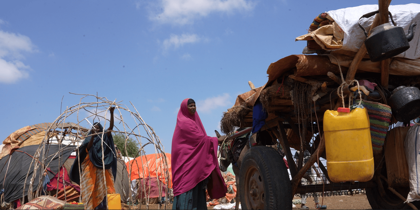 En kvinna i ett flyktingläger står bredvid en åsnekärra.