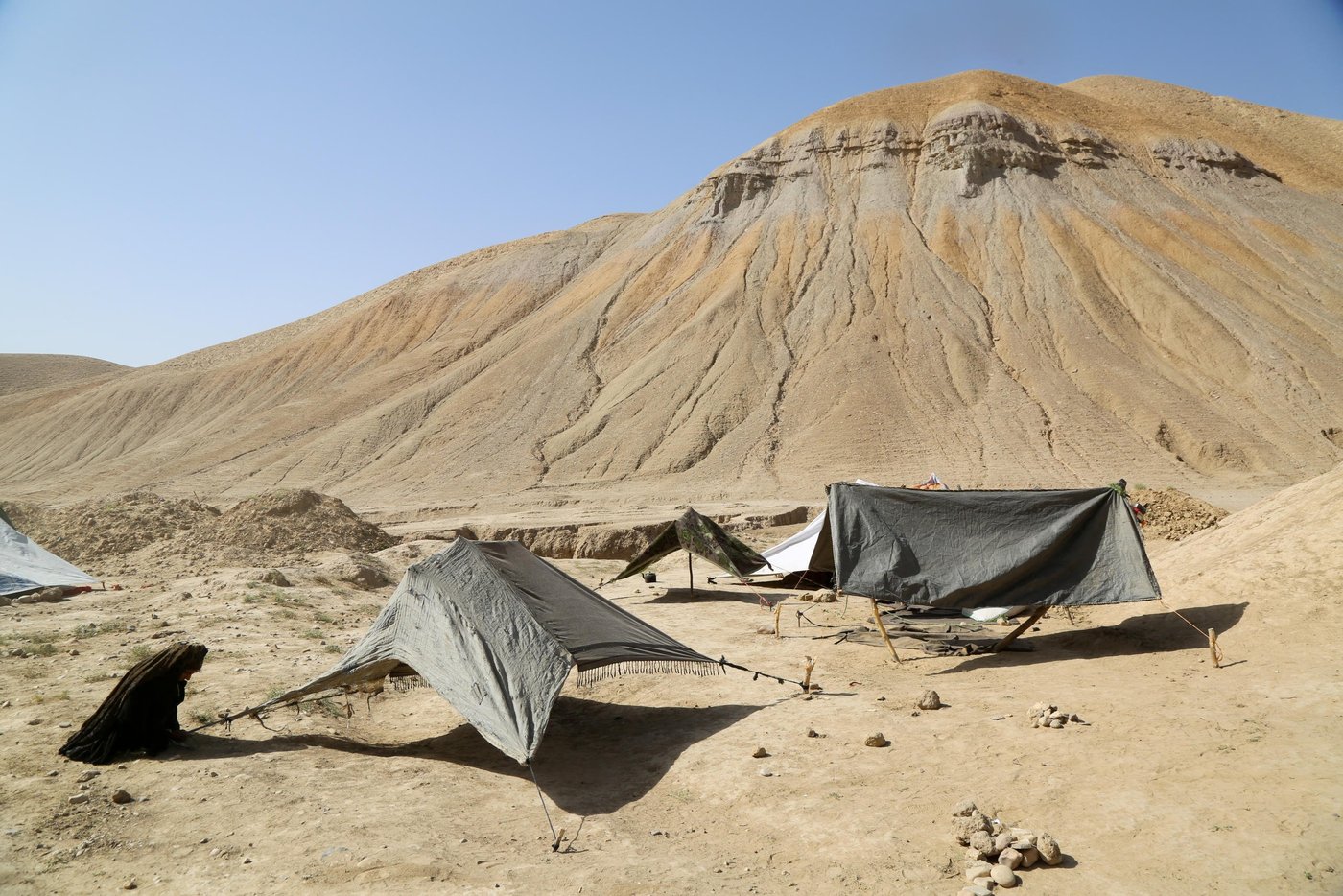 Displaced woman erecting her makeshift tent at Sanjetak IDP settlement.
Children at Sanjetak IDP settlement. Sanjetak IDP settlement located on the ring-road to Faryab and Balkh. Many people were moved from Qala-e-naw surrounding areas like Kharestan. Families moved in different dates but many were displaced in their villages before coming here. Some of the families were moved from Shamali Darya to here. Families interviewed said that they have come here due to gov’t encouragement.
Woman we spoke in this settlement said she had lost her there-months daughter due to cold and respiratory causes and allegedly many babies were died due to cold. Families were asking for shelter, WASH and food assistance. The families here are provided with bag of flour and water trucking. Photo: NRC/Enayatullah Azad