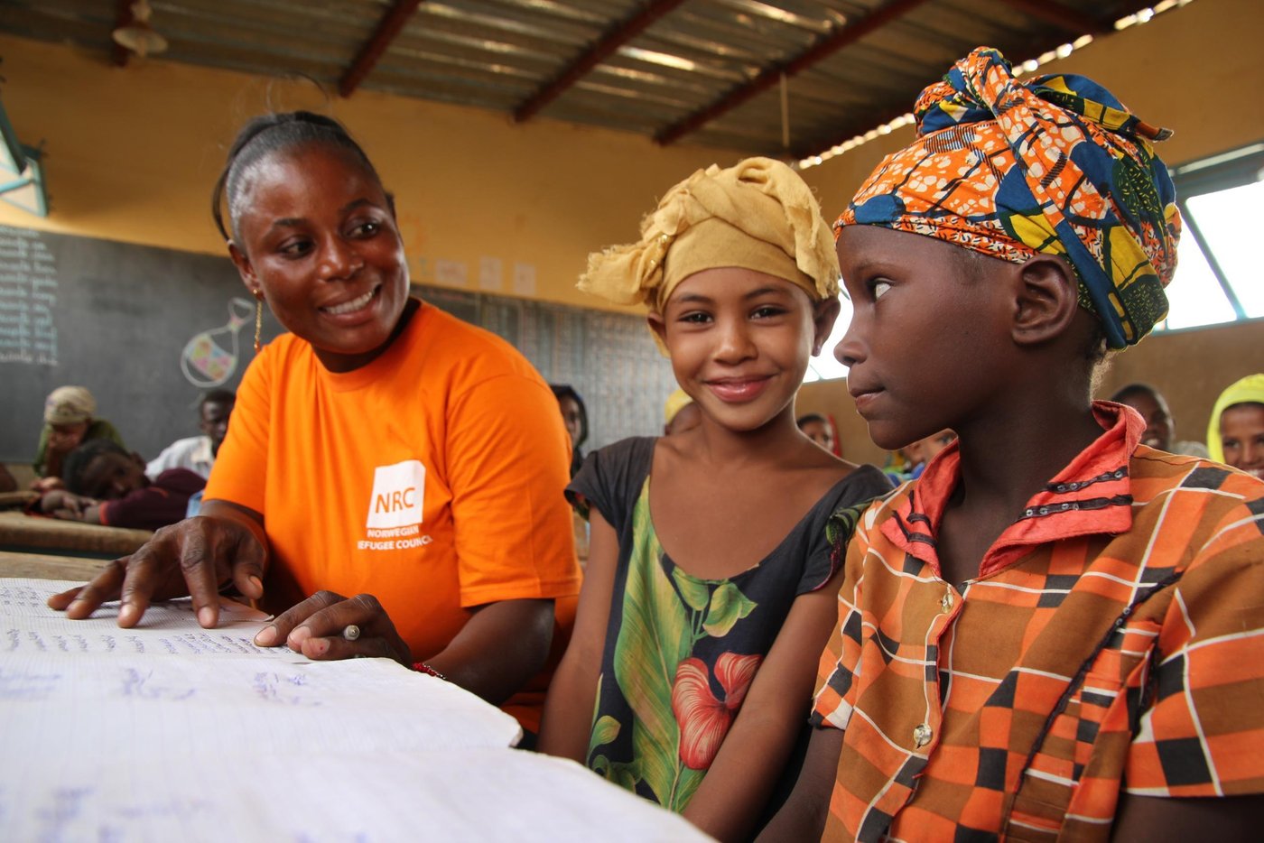 NRC education assistant Diallo Fatimafa  together with Salamate Sambo (12 years old with yellow scarf) and Sada Walette Al Houssein (8 years old with colourful scarf).

 Education:
 NRC has through the years provided different types of education programs. In 2013-2015 NRC ran an education project in the Mentao refugee camp comprising a catch-up programme for children of school going age who have been forced to drop out of school. NRC also had  a YEP program (combining literacy educational and learning crafts) for youths between the ages of 15 to 24 who can no longer make in into the normal school system. 163 pupils completed the catch-up programme while 105 youths completed the YEP programme   

Now NRC is providing education for smaller children in the Goudebo camp; Ecole Primaire de Goudebo has between 800 and 900 pupils aged from 6 to 12 years, divided in six grades. The number of pupils differs with families trying to return to their country of origin. Return programme is facilitated by UNHCR.

Most of the pupils are refugees, but the school also has some pupils from the host community.

There are 6 grades at the school. In the first two years (CP 1 and CP 2), there are two teachers in each class. Because the school language is French, and many of the refugee children do only speak local Tuareg dialects, they need help for translation to be able to follow the education. (Official schools in Mali is also teaching in French)

NRC target that 50% of all pupils should be girls is met in the vast majority of the classrooms. The age of the children in each class differs. Most of the children arriving in the camp have never gone to school before, so they have to start in the basic class regardless of their age. 

Most of the pupils have books to write in, but in a few classes the pupils still uses small wooden boards and chalk.

Photo: NRC/Ingrid Prestetun