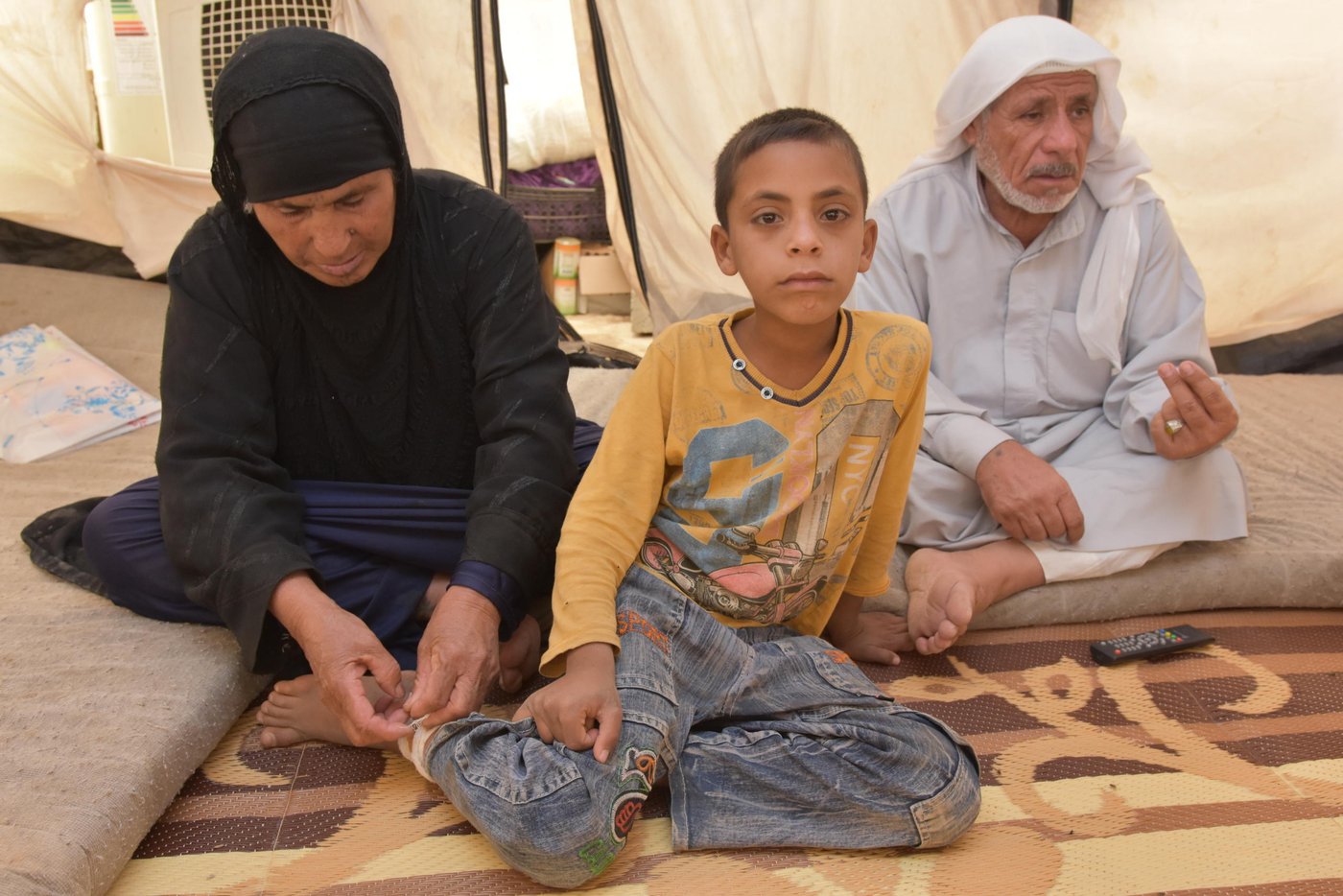 Najma Zarzor Hassan (born 1954) and Fathi Jasim Mohammad (born 1946) with four of their grand children. The three boys are brothers, the girl is the daughter of another son.
Azer (8) (yellow sweater, sitting with his grandmother) is Ahmed’s cousin. Azer is one out of many Iraqi children who has suffered tragic losses. For two years from 2014 - 2016, IS controlled the place the family comes from.
“ISIS blew up my school, I want a new one”, the little boy says. It is in November 2016 and the 8-year-old is living with his grandparents in Debaga camp 2. The grandparents are also taking care of Azer’s two brothers Nehro (5) and Fathi (10) (also in the picture). The boys’ father was killed by ISIS, accused of collaboration with the Iraqi military. Their mother was killed in a bomb blast four months ago, when military forces attacked the village in order to free it from ISIS. Azer was injured in the same bomb explosion that killed his mother.
His grandmother carefully changes the bandage on his right leg. “He got treatment here in the camp yesterday. He still has several fragments from the blast in his leg and three in his head”, she says, pointing at the blast injuries. “Look, here. Here. Here. They are so many of them.”
“My other son crossed a minefield close to the village. He lost his eyes. The area around the village is full of booby traps”, says grandfather Fathi.
Fathi describes how ISIS killed innocent people with horrible brutality, and says that when the Iraqi army withdraw and ISIS took control, it got worse. “They started to be very hard with us. They would even kill kids like this little ones.“
“They, ISIS, are deprived from any kind of human feelings and standards. A life has no value at all. I am 70 years old and even in my generation we have never seen this evil. They have no human principles, no religion. And they come from all countries“, he says.
“A smoker could not smoke a cigarette, men had to grow a beard. Pants had to be long, reach to your legs. All breaches on the rules were punished. The provided each family with only 5 kilo of flour, that is nothing.
“Since we came here, it was better. After the airplanes came to liberate us. The Army advanced. Our areas being liberated. There was some losses, but it is better than being under ISIS control.”
“At the moment there is no future for my grandchildren. As long as me and their grandmother we will take care of them. My son who was killed was educated and graduated, he worked with us at our farm. We were farmers. Now we have nothing and we are doing nothing“, says Fathi Text / photo by Hanne Eide Andersen/NRC