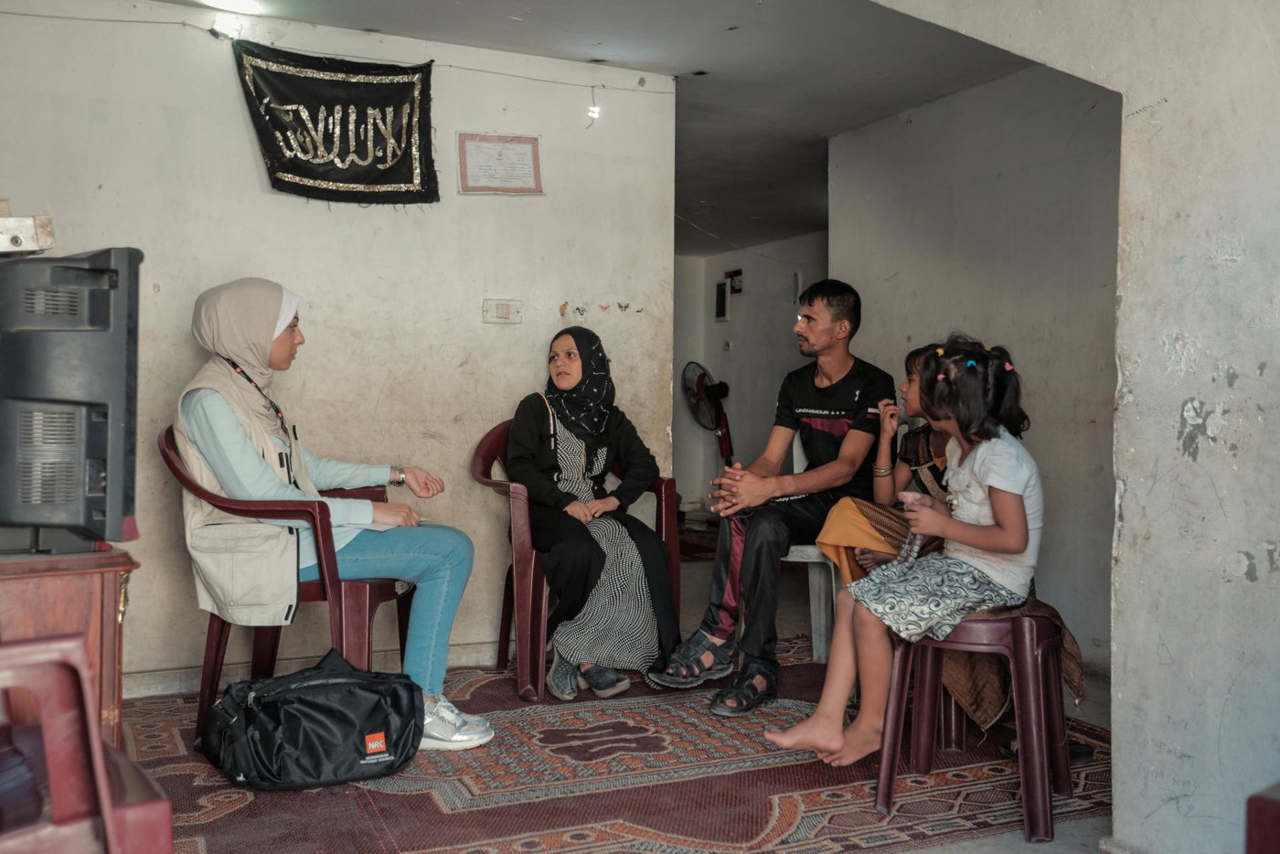 NRC Shelter Technical Assistant Aya Abu Ramadan (left) meets the Al Zaharna family inside their rented apartment. To her immediate right is Eitidal, 30, her husband Medhat, 33, Remas, 7, and Layali, 11.
“Just before NRC’s support, the landlord had warned us that we have a short period to search for another house, as we had four months of unpaid rent,” said Eitidal. “We remain worried about what will happen when the six months of cash for rent assistance ends and fear eviction.”
Eitidal and her family have been renting their home in Jabalia for the past year. Less than half of households surveyed by NRC have lived in the same place for more than one year, due to their inability to pay rent. 
The apartment’s poor condition, limited ventilation, mice, and cockroaches are still better than living on the street. 
Out of the 522 households, 23 per cent live in homes that fail to meet the minimum standards set by the Shelter Cluster, an inter-agency mechanism that coordinates the humanitarian shelter response, while 4 per cent live in informal shelters such as storage units, which lack even running water and sanitation.
The family has been evicted twice before over accumulated rental debts. Their previous landlord cut off their electricity, threw their furniture out on the street, and submitted a complaint to the police. 
Too often, Eitidal says, she finds herself without food for her children. In May, her daughter, Rimas, tired and hungry after school exams, ate leftover food thrown away by a nearby restaurant, and had a nasty bout of food poisoning.
Since hearing of the story, the restaurant owner has given the family cooked rice for free, and whenever Eitidal has nothing to feed her kids, she sends them there to eat. Other times, Eitidal’s husband brings home spoiled vegetables from the market and every once in a while they go over to their relatives for meals.  
Even drinking water can be hard to come by. 
“We do not have either a water tank or a jerry can,” said Eitidal. “I send my daughters to the supermarkets to fill 10 water bottles at a cost of one shekel [US$0.28]. Sometimes we do not have one shekel and must hope on the goodwill of neighbours.”
According to the 2018 food security survey by the Palestinian Central Bureau of Statistics, 68.5 per cent of Gaza’s households are food insecure, with 47 per cent severely affected.    
Eitidal’s family receives cash assistance of 1,000 NIS (US$284) from the Ministry of Social Development every six months and UNRWA food vouchers every three months. Eitidal has had to sell the food items she purchases with these vouchers for half their worth to have money for medicine, gas, and other basic necessities. Otherwise, they rely on the goodwill of relatives and strangers to survive.
Around six months ago, Eitidal, in desperate need of money, promised the same food items she was due to receive to two people. When she was unable to provide the second person with the items, he made a complaint to the police.  
“The police came to take my husband to jail, and my daughters started to cry,” said Eitidal. “Since then, they have become terrified every time they see a police officer.” 
Eitidal’s husband spent 21 days behind bars. 
More recently, Eitidal signed a promissory note (a promise to pay outstanding debts by a fixed date) for debts in the amount of 220 NIS (US$63) to a supermarket owner, who involved the police to force the family to pay the full amount in installments.  
“The day we receive the cash assistance from the Ministry of Social Development is the worst ever,” said Eitidal. “All the lenders come asking for their money.”
Photo taken on 21 August 2019, Jabalia, northern Gaza.
Photo: Ahmed Mashharawi/NRC