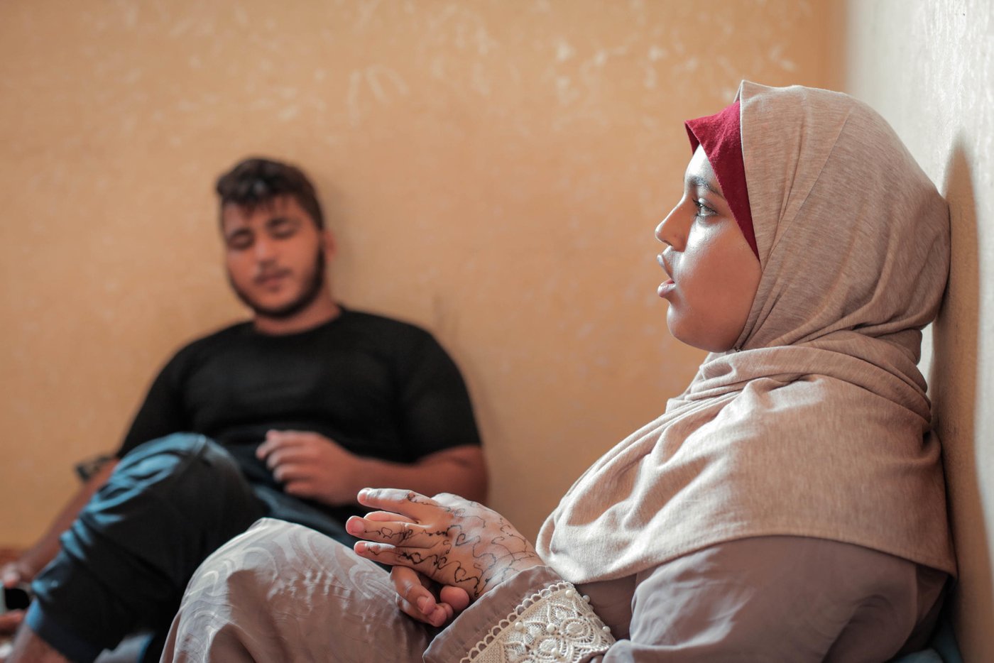 Diana Murad, 18, and her brother Mohammed, 15, in the background in their rented apartment in Al Shati Refugee Camp in Gaza City.
Diana sustained shrapnel wounds to her left arm and thigh in 2018 while taking part in the Great March of Return mass protests on Fridays along Gaza’s perimeter fence with Israel.
In March this year, a tear gas canister struck her in the right shoulder. While Diana’s father looked for her amid the crowds, he fell to the ground with a bullet wound to the leg. Complications arising from diabetes and kidney problems have stalled his recovery.
All five siblings dropped out of school because of the number of times they have been forced to move after getting evicted from their home, as well as lack of funds for school fees, uniforms, and transportation. Ali and Mohammad, 15, completed first grade only; their siblings Jenin, 17, and Saed, 16, made it to second grade, and Diana graduated from fifth grade.
Photo taken on 21 August 2019
Photo: Ahmed Mashharawi/NRC
