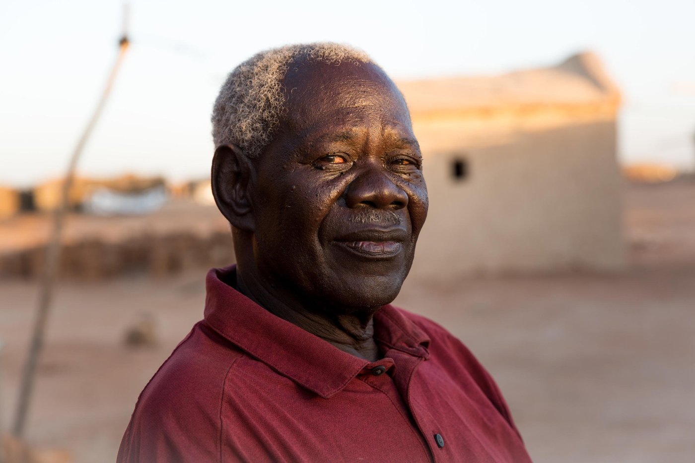 Anglo Woku never imagined he would be considered a refugee in Sudan in his twilight years. Especially since he left the Southern part of the country for a better life almost 50 years ago.
“I escaped in 1969, shortly after the civil war broke out. I ended up in Khartoum. I was working for the military. I was married, had a family and friends. Sudan gave me a good life,” he said.
The conflict between North and South raged on for 22 years until a peace agreement was brokered in 2005. Then in 2011, the people of the South voted for independence and South Sudan, the world’s youngest nation, was born.
This new dawn however caused all sorts of legal uncertainties for the South Sudanese living in Sudan, particularly in the years following independence.
“I lost my Sudanese identity,” Anglo, 78, explained: “I went from being a public servant to a refugee.”
In 2011 following the independence of South Sudan, Sudan passed laws that had a detrimental impact on the identity of people with Southern heritage.
They automatically lost their Sudanese nationality and were now considered South Sudanese. Even their children, despite being born and raised in Sudan, were given a new nationality. Many people had no intention of returning to South Sudan, a country, largely unknown to them and this created a legal dilemma on questions around their legal status. 
Under the Four Freedoms agreement signed in 2012 between the government of South Sudan and Sudan, South Sudanese were to be granted freedom of movement, residence, economic activity and the right to acquire and dispose property. They were also awarded prima facie refugee status, however the legal status of those who lost their Sudanese identity following the cessation, but with no intention of returning, remains unclear.
Some however made the decision to leave for South Sudan both spontaneously or with the assistance of the UN through facilitated returns.
As part of the organised returns, those willing to repatriate were assembled at departure points. However, in 2013, conflict erupted in South Sudan and the operation was stalled leaving thousands of South Sudanese in limbo and stuck in departure points, to this day.
These departure points, now known as Open Areas, are home to over 31,000 South Sudanese living in nine Open Areas across Khartoum. Anglo is among those languishing in these areas with no rights or access to a decent standard of living.
While registration efforts continue, it is estimated that there are around 154,700 refugees living in nine Open Areas including Um Badda, Jabal Aulya and Sharq El Nile across Khartoum state. They make up approximately 55 per cent of the overall South Sudanese refugee population and are among the most vulnerable members of Sudanese society.
Life is tough in the Open Areas and thousands have limited access to food, water, healthcare or livelihoods. 
“I found myself jobless and homeless with no rights, no identification and I have been here ever since,” Anglo revealed further.
Fondly known as ´the Sultan´, the name given to well-respected leaders in the community, Anglo went from the upper echelons of Sudanese society to being exiled to a dusty, sparce flat land called Nivasha on the edge of Khartoum’s city limits. 
He and thousands more live an invisible existence here, virtually hidden from the rest of the Sudanese population who struggle on with life in a country buckled by years of oppression, debt, government corruption, international sanctions, recurrent drought-related famines and humanitarian chaos. Out of sight and out of mind seems to the policy for urban refugees in modern day Khartoum.
“I did not want to become a refugee. I worked hard as a citizen but this happened. My children have moved back to South Sudan, but my wife is here. My children have jobs and they are safe. We had planned to move back there but there is no way out now. I have no money and we are struck here.”
Like several others, Anglo is a trapped in an administrative quagmire that no organization or agency has the full funding, capacity or support to resolve.
The Commission for Refugees is the body mandated to manage refugee affairs in-country including registration and refugee status determination. It is funded by UNHCR, which maintains a supervisory role, is currently dealing with a backlog on registration. Access to documentation remains a key challenge for all unregistered refugees. Biometric registration is ongoing however it will take time before the backlog is cleared.
The winter sun is setting as we arrive at Nivasha settlement and paints a golden syrupy hue over the far out and forgotten community.
Terra cotta-coloured cuboid homes line the vicinity like blocks on a Tetris game. Curious heads peep out from glassless windows of makeshift shops, indicating some market infrastructure but nowhere near enough to serve the disadvantaged population.
Bells tinkle from under the throats of overburdened donkeys carrying the only available water to the residents. A teenage boy rides on top and raises his thumbs to smile as the camera flashes and lights up the expansive area that will soon be in plunged into darkness.
There is limited electric, running water, and food scarcity plays constantly on the minds of mothers desperate to feed their growing children.
“There is no food,” said 70-year-old grandmother Apuk.
“We are constantly hungry. I have never known hunger until I came to these settlements,” she said.
A handful of local agencies including WFP offer humanitarian assistance to the 11,000 people of the settlement but there are virtually no income-generating activities available to provide a sustainable away from a reliance on aid.
As a result, many residents venture into the nearest neighbourhoods or markets for daily work opportunities. Men find casual labour while the women find cleaning or housekeeping jobs.
“My daughter when she gets work, provides around 50 Sudanese pounds per day (less than a dollar). If we get money, we get a meal once a day. But if she finds no work, we have to search for food in the night to ensure the children get something to eat,” Apuk said.
“We often come home with nothing.”
Like many vulnerable communities around the world, the Covid-19 pandemic has had a crippling economic effect on people fiercely reliant on daily labour wages.
Restrictions and lockdowns forced the city to close and dried up the only work opportunities available to men and women living hand to mouth. The cash-dependent people of Nivasha are no different to the cash-dependents of Naples, Nairobi or New York. Pandemic poverty affects all.
With no adequate health or sanitation facilities around, Nivasha is a welcome host for coronavirus among other diseases. And if anyone is sick, there is no ambulance to take them to a hospital. The nearest hospital is miles away and the only way to travel is an expensive and unaffordable taxi or motorbike ride.
With the recent inflation rate, certain food commodities such as red meat, dairy products and fish are also expensive. Everything is expensive in economically-fragile Sudan.
As Anglo points out, people need more than subsidies to be able to afford to eat, they need opportunity.
“This land is good. It can be productive for food with the use of small backyard land, but the community does not have the support to start food production activities,” he explained.
“If they had their own vegetables, they could eat them and sell them. There are many women here that are farmers. They know what to do. They would like to start farms or shops.”
Apuk reveals that she grew up on a farm in South Sudan and remembers her young life well.
“We had a good life. We had food, plenty to eat. We were fishermen. I miss the taste of fish, I used to eat it every day,” she smiled.
“I feel safe in Sudan but I just want my children to eat. I want them to have some life. I am old but they are not. I have lived and worked in Sudan, but I would like my community to live better,” she said.
Anglo admits life is not what he expected it to turn out but finds comfort in the many friends he has found in the community. As he talks, several men of various ages gather around him in a brotherly circle. “He is a good man,” says George Allam Lolika-Khalil, the Sultan of another camp, “he cares for the community. He tries to make things right for us especially the children.”
Anglo believes that with the new democratic government, Sudan has the potential to grow but he would like to see the refugee community better served and no longer forgotten.
“If they don´t provide livelihood opportunities or training. We will just waste away. We are now known as refugees but many of us have lived here all our life and we just want to continue living without struggling. We just want to feel settled in the country we have always called home,” he said.

Photo: Ingebjørg Kårstad/NRC