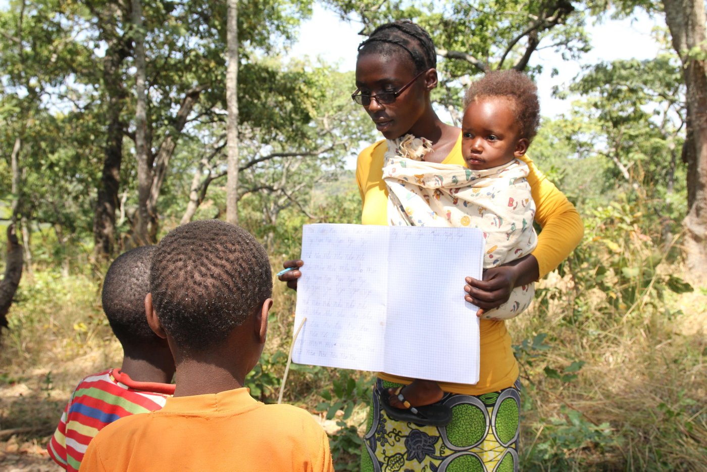 Violette arrived in Tanzania in January 2017. She started teaching in May 2017. Now she teaches Class Two. Her class has a total of 50 pupils. However, the attendance on 14th June was only 13. Reason for the poor show? Lack of books and pens, together with the reason that the pupils were escorting their parents to the food distribution.
A slim and tall young lady, Violette has one child, Bijou Iratabara. The girl’s name means ‘God comes to help people in need’. She had longed for a child for many years and she feels that the Almighty God had finally come to her rescue. Bijou is now two years old. Bijou means gift in French. She is the gift that God has granted to Violette.
Violette originates from Gahandu Commune of Makamba Province in Burundi. Her story from Burundi is filled with traumatizing episodes. Her husband was abducted one evening by members of a dangerous militia group. He had received death threats from some people a few weeks earlier, because of his political affiliation. She fears that the militiamen might have killed him and dumped his body in a river or forest. During those times, it was common to come across corpses of dead people dumped along the streets or washed down the river.
What motivates her to do her job despite hardship? “I am happy when children learn to read and write. It is very fulfilling to see children make progress in their schooling. Now they are trying to catch up, I know that they will succeed, despite the lack of adequate learning materials”, she says.
She always brings her daughter to school. Most times, she is forced to teach while carrying her. This is because she does not have any helper at home. Fortunately, Bijou is always calm and unless she is hungry, she prefers to mind her own business most of the time. There is another female teacher who comes to help in case she needs attention. Violette says that she wants to remain in Tanzania together with Bijou, unless refugees are forced to leave by the authorities.
Quote from violette (June 2017)
“I decided to teach children so that they get knowledge like I got.”
“I teach other children so that life does not stop even though we are in camps, it should continue, they should know how to read and write.”
“I fled before starting to teach. I had just finished my studies. Then the war started before I started teaching children, but I had finished.”
“I fled because my husband, the father of my child, had been taken away because he was not belonging to ruling party. I grew up as an orphan. Whenever I went to my friends, they continued to come looking for my child wanting to kill her. I decided to come here requesting to become a refugee so that my child could live.”
“I like to give knowledge to other children because education is what a child should be given in life.”
“Education is the pillar of development to a child.”
“I like to give children education so that they know how to read and write. Even though they are refugees when they go back to our home they will know how to read and write. They will develop the country.”
“It is difficult to teach. Children do not have books, pens, they don’t have classrooms, schools. A teacher does not have means of transport, bags to carry exercise books on which she writes. But we continue to sacrifice although it is difficult.”
“I live alone. I don’t have anyone to help me taking care of my child. But I continue to volunteer, helping children of my friends, children of my country. We are not paid, we don’t get a salary. Although it is difficult, I continue giving them education so that they also get knowledge.”
“I wish my child, wherever she will be, if she gets education she becomes a journalist.”
“I like to give children education, I like to volunteer. Giving knowledge, giving to other children and my child. When they go back to Burundi they have knowledge and they develop our country.”
Photo: NRC/Ingrid Prestetun