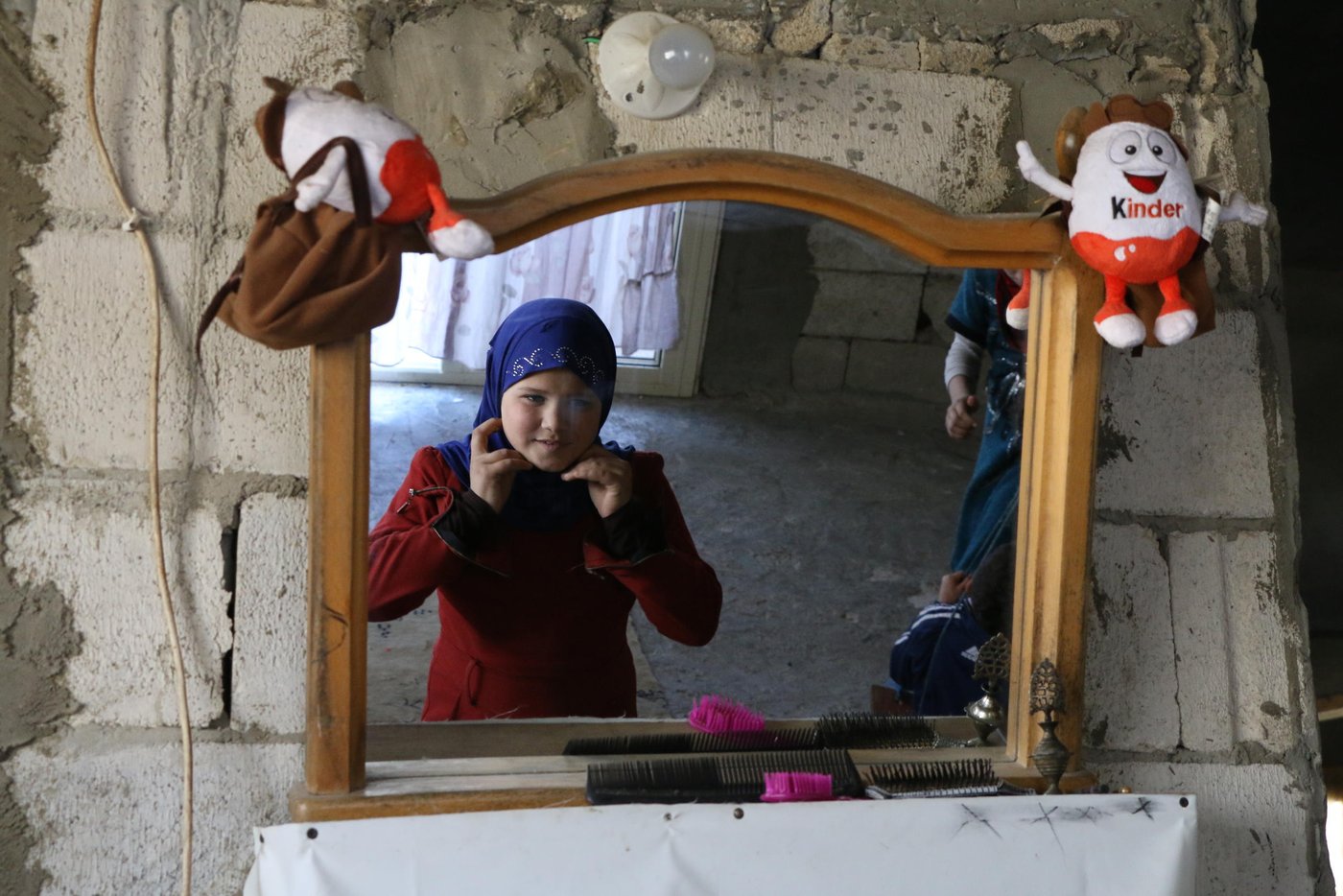 Sarah, 10, is fixing her veil on the mirror hung on the wall of their new shelter.

Photo: Nadine Malli/NRC