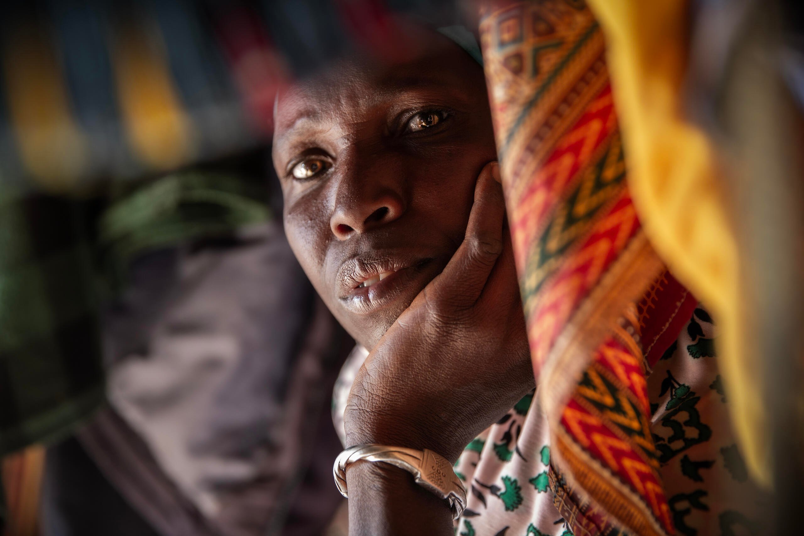 Portrait of a woman resting her head in her hand, surrounded by colourful fabrics.