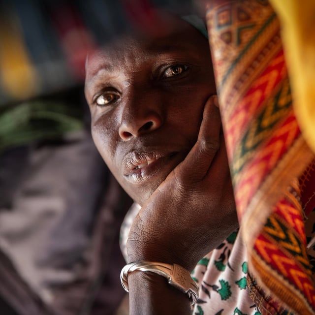 Portrait of a woman resting her head in her hand, surrounded by colourful fabrics.