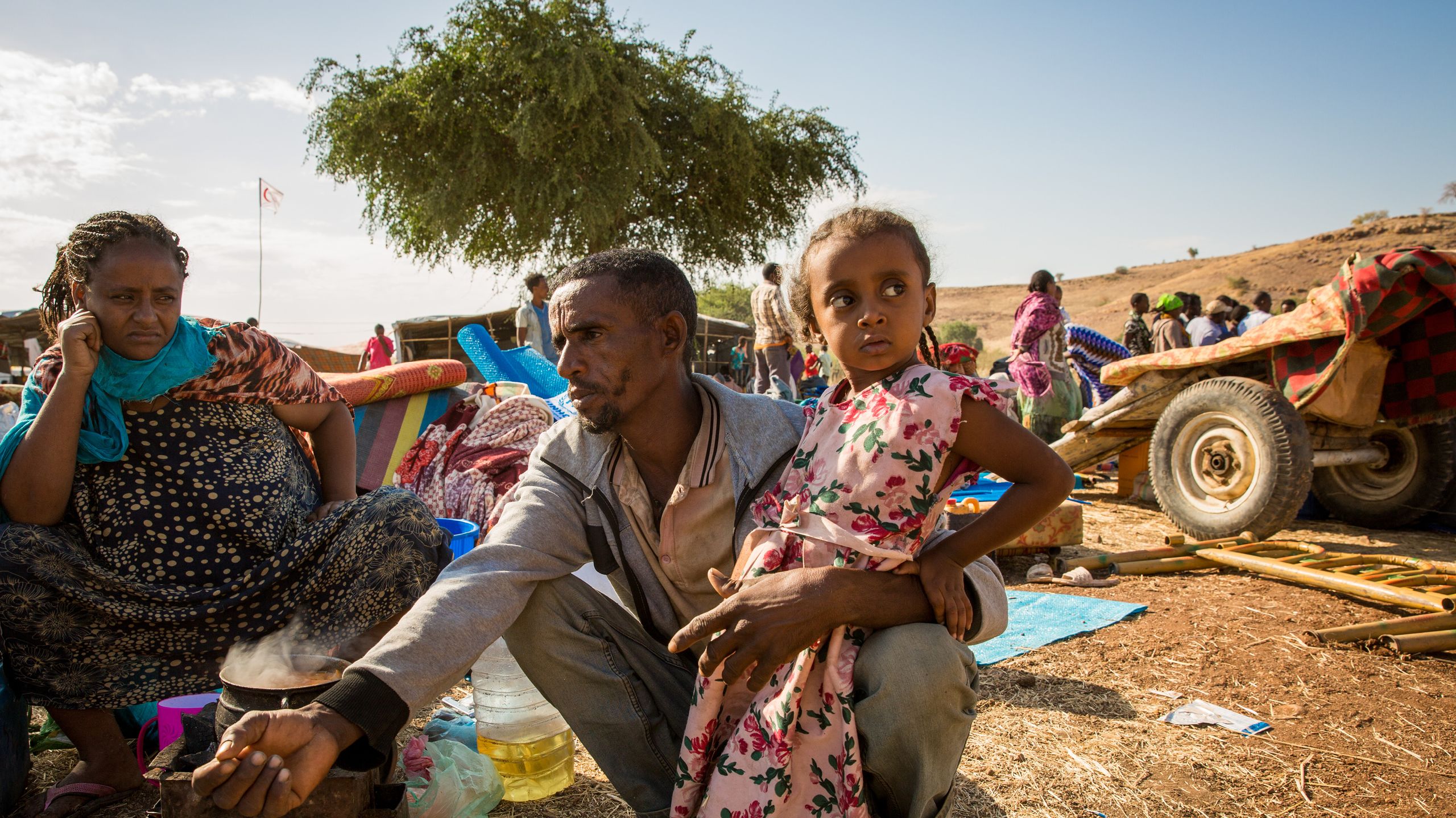 En far sitter på bakken i en leir. Datteren hans lener seg inntil han.