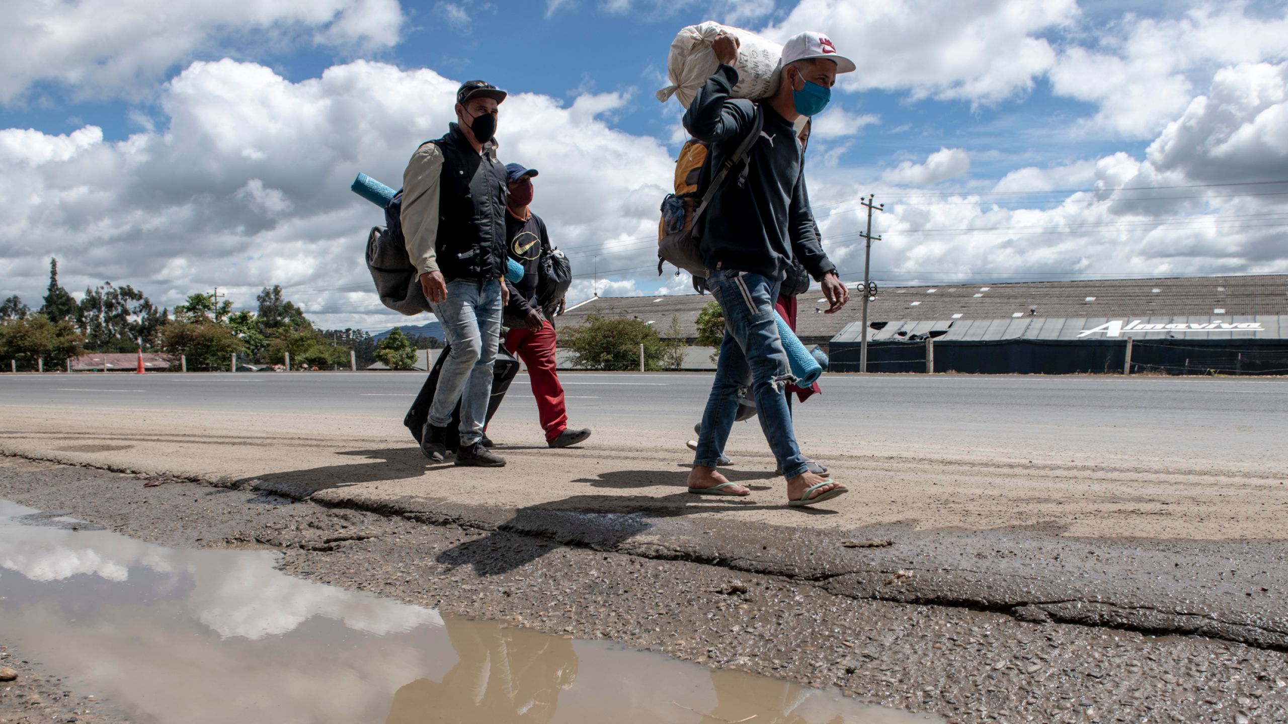 En gruppe går langs veien. De har store sekker med eiendelene sine på ryggen.
