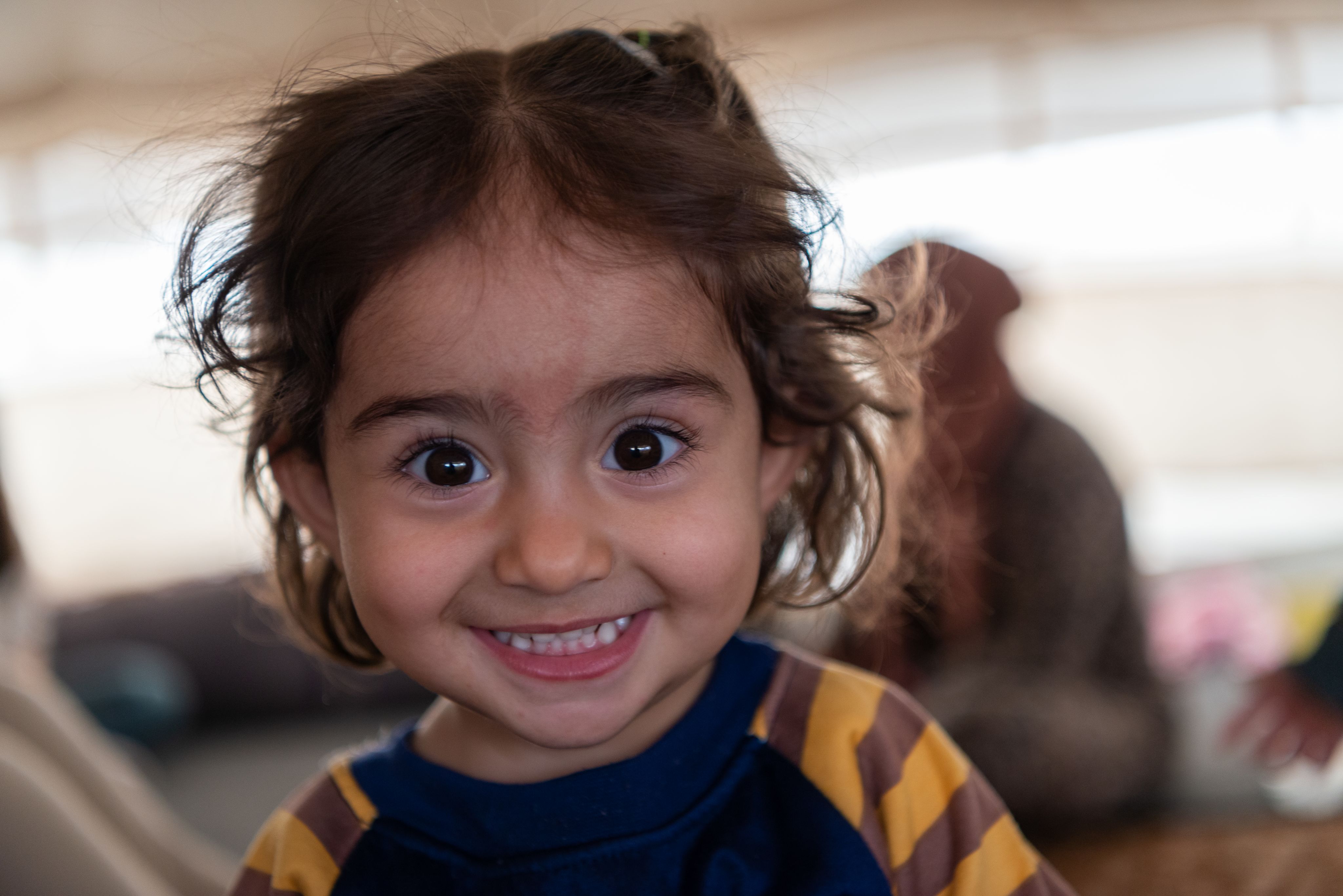 En liten jente smiler som en solståle til kameraet.