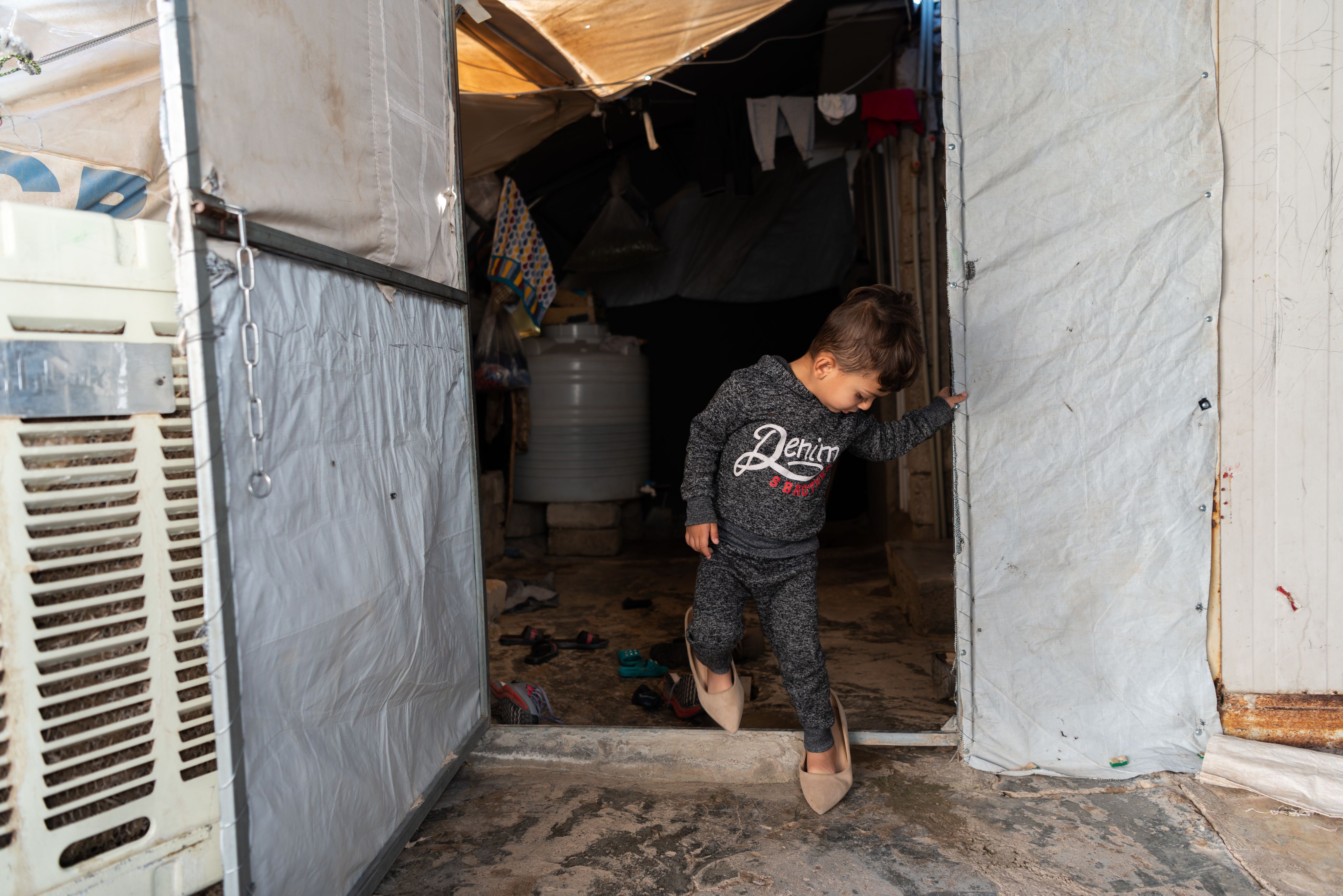 En liten gutt har lånt mammas sko. Han er på vei ut teltdøren.