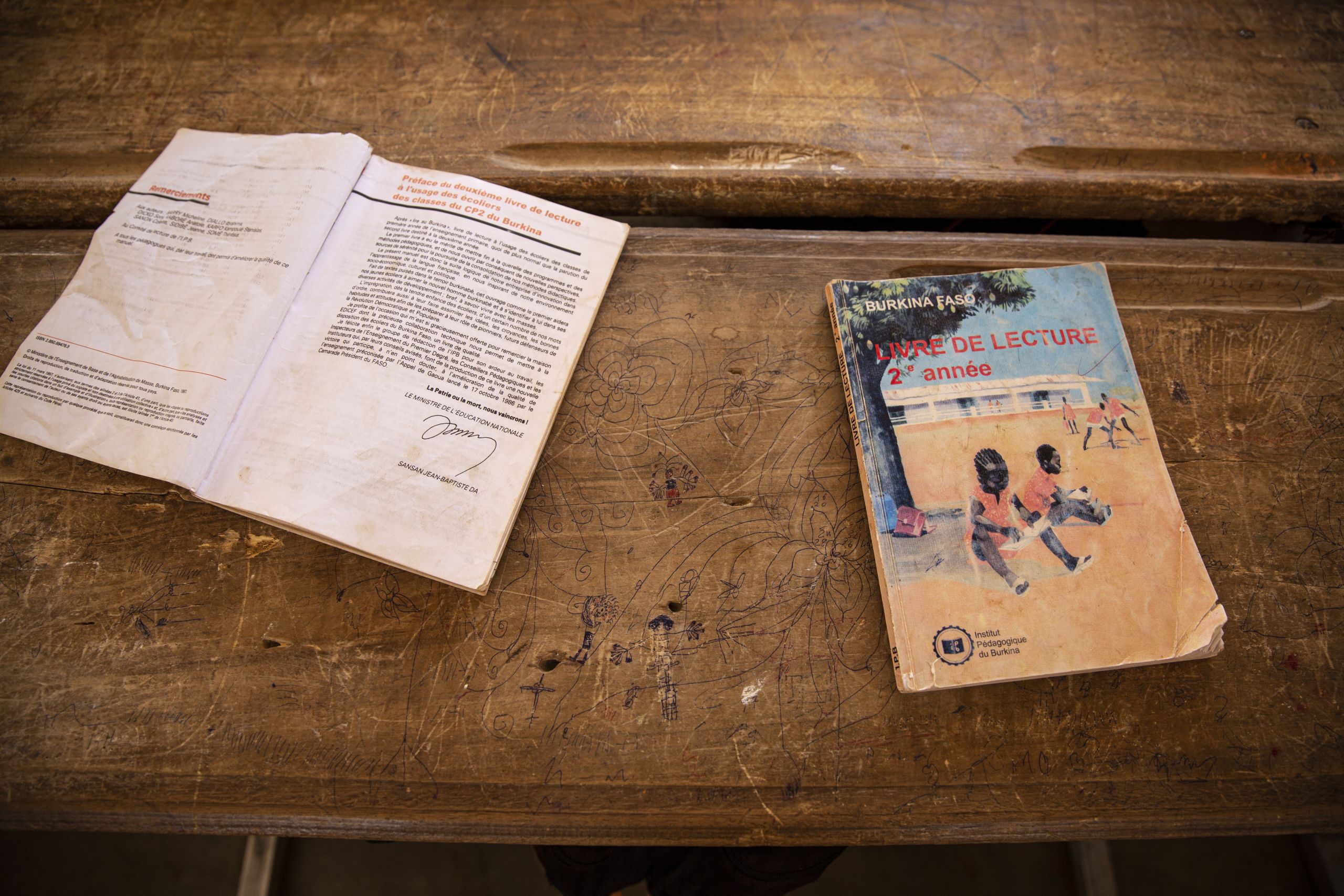 To lærebøker ligger på en pult. Den ene er åpen, mens den andre er lukket. På forsiden er det tekst på fransk og en illustrasjon av to barn som leker under et tre.