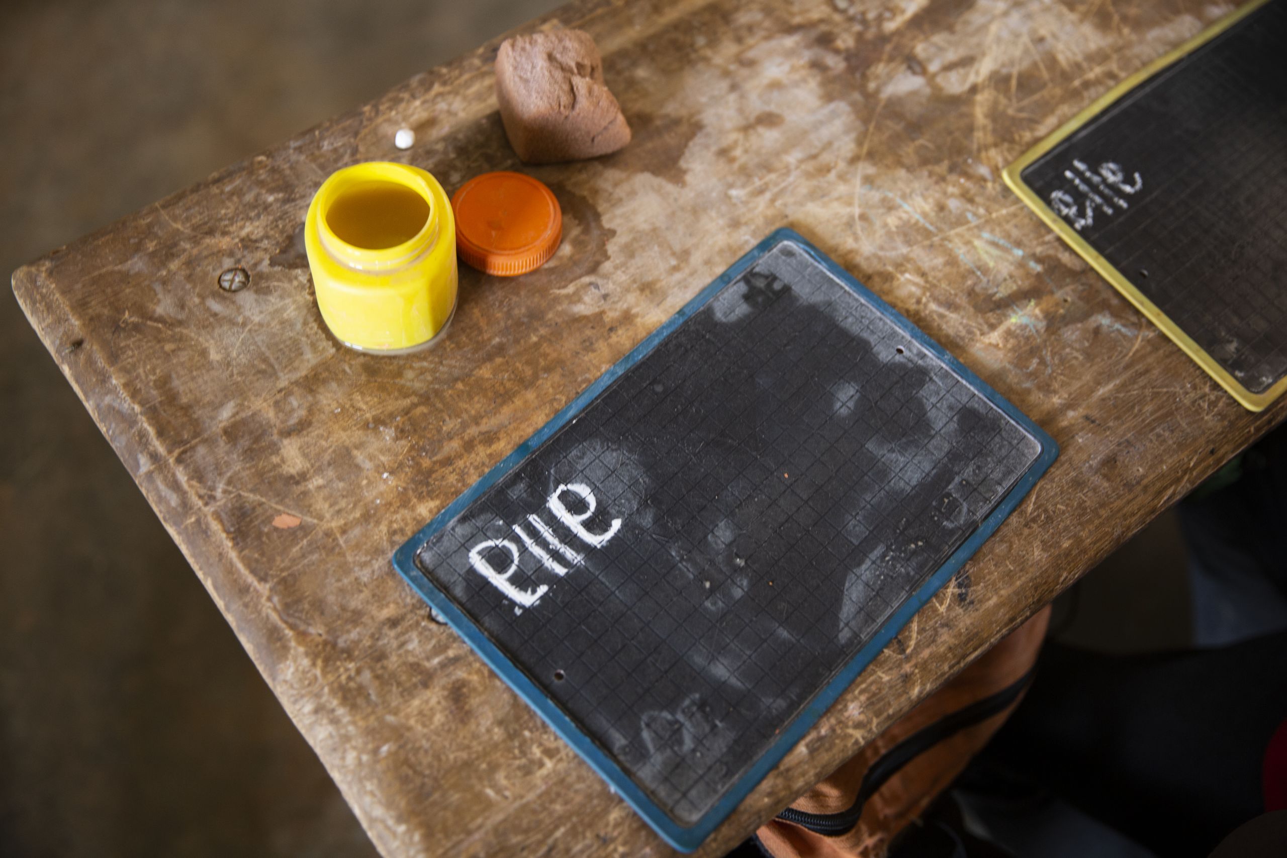 Et lite tavlebrett ligger på en pult. "Elle" er skrevet med kritt. Ved siden av brettet står en beholder med vann og en svamp.