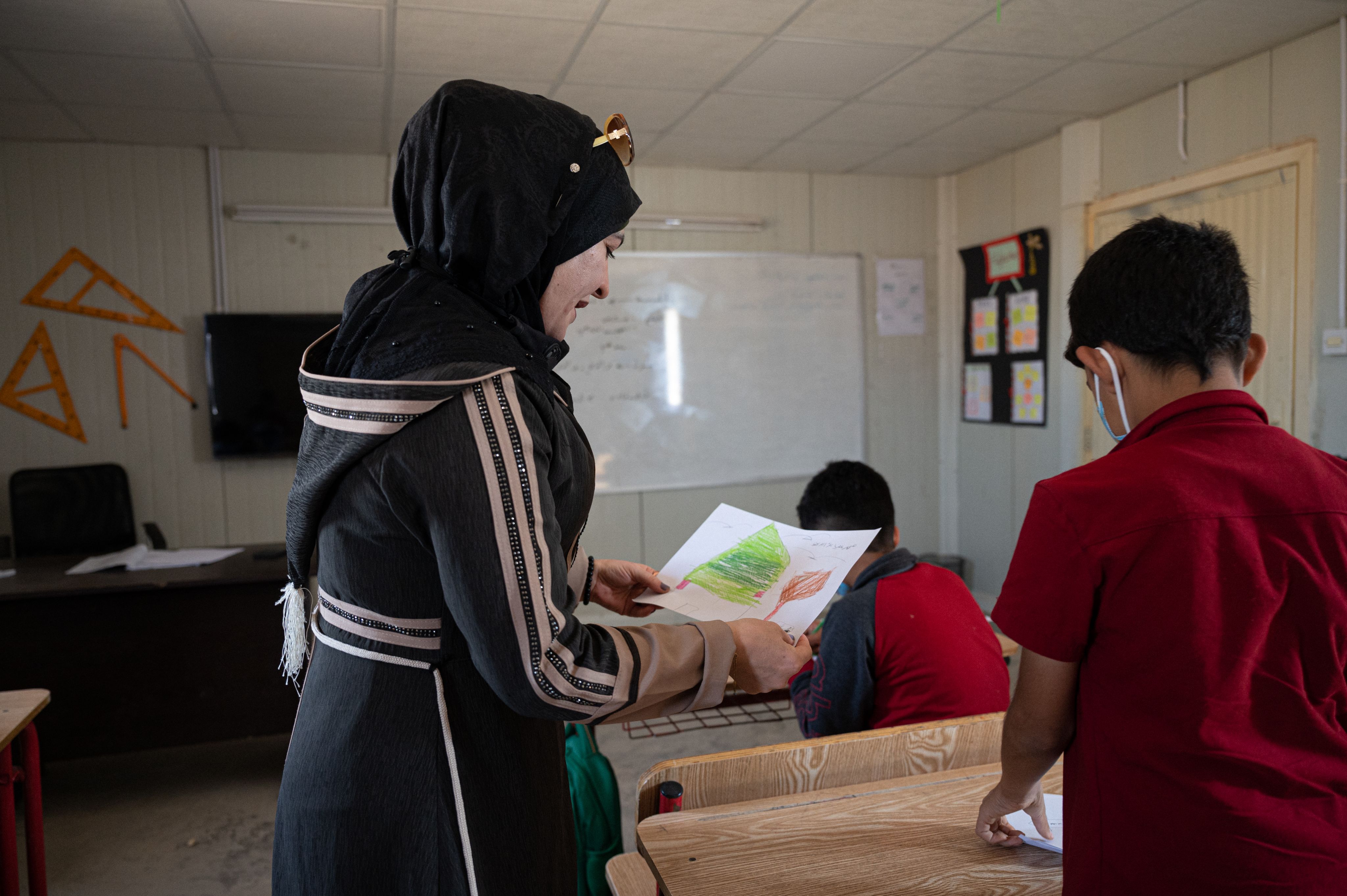 A Syrian teacher looks at the drawing of one of her students
