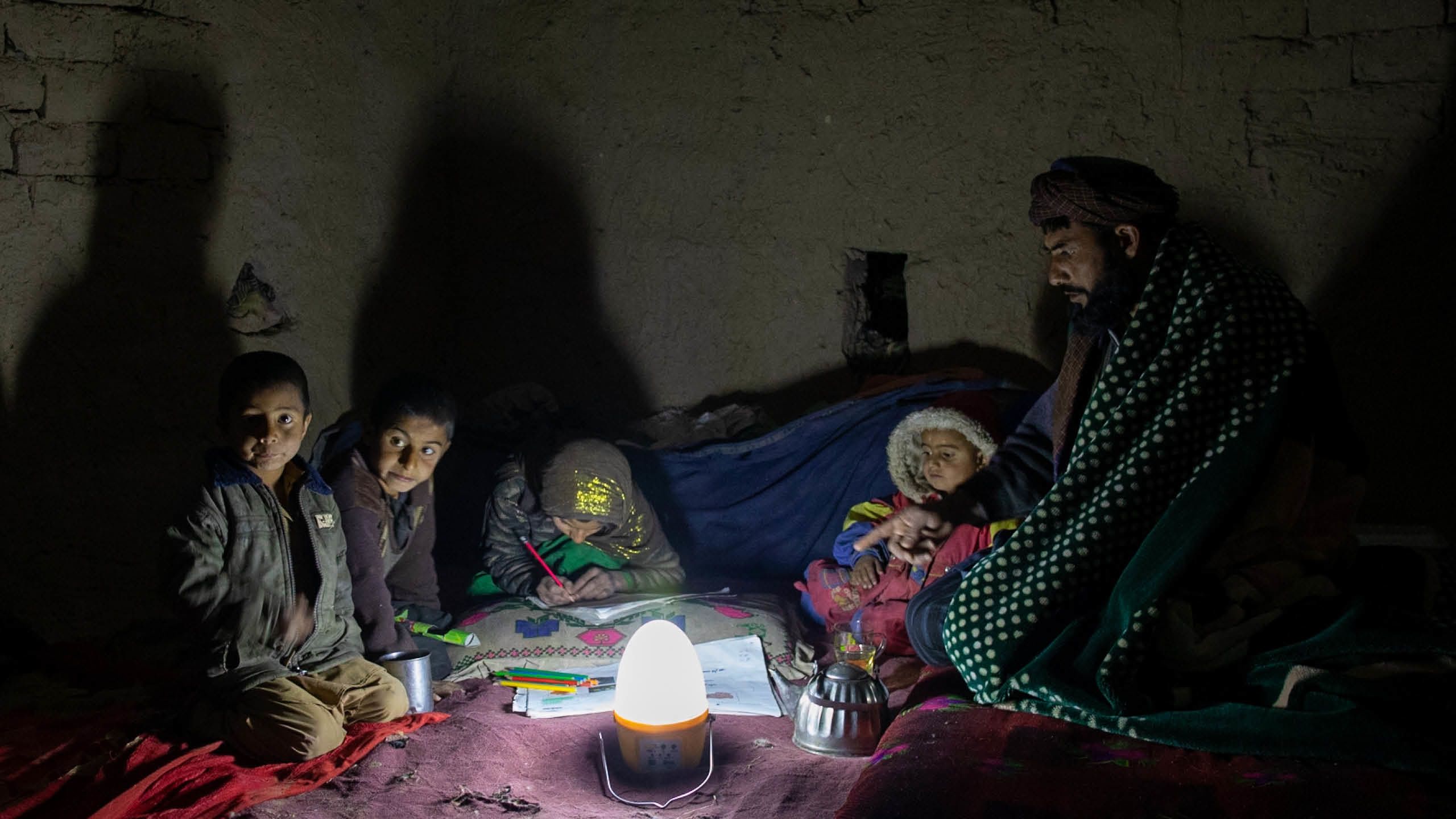En far og hans fire barn sitter rundt en solcelledrevet lampe.