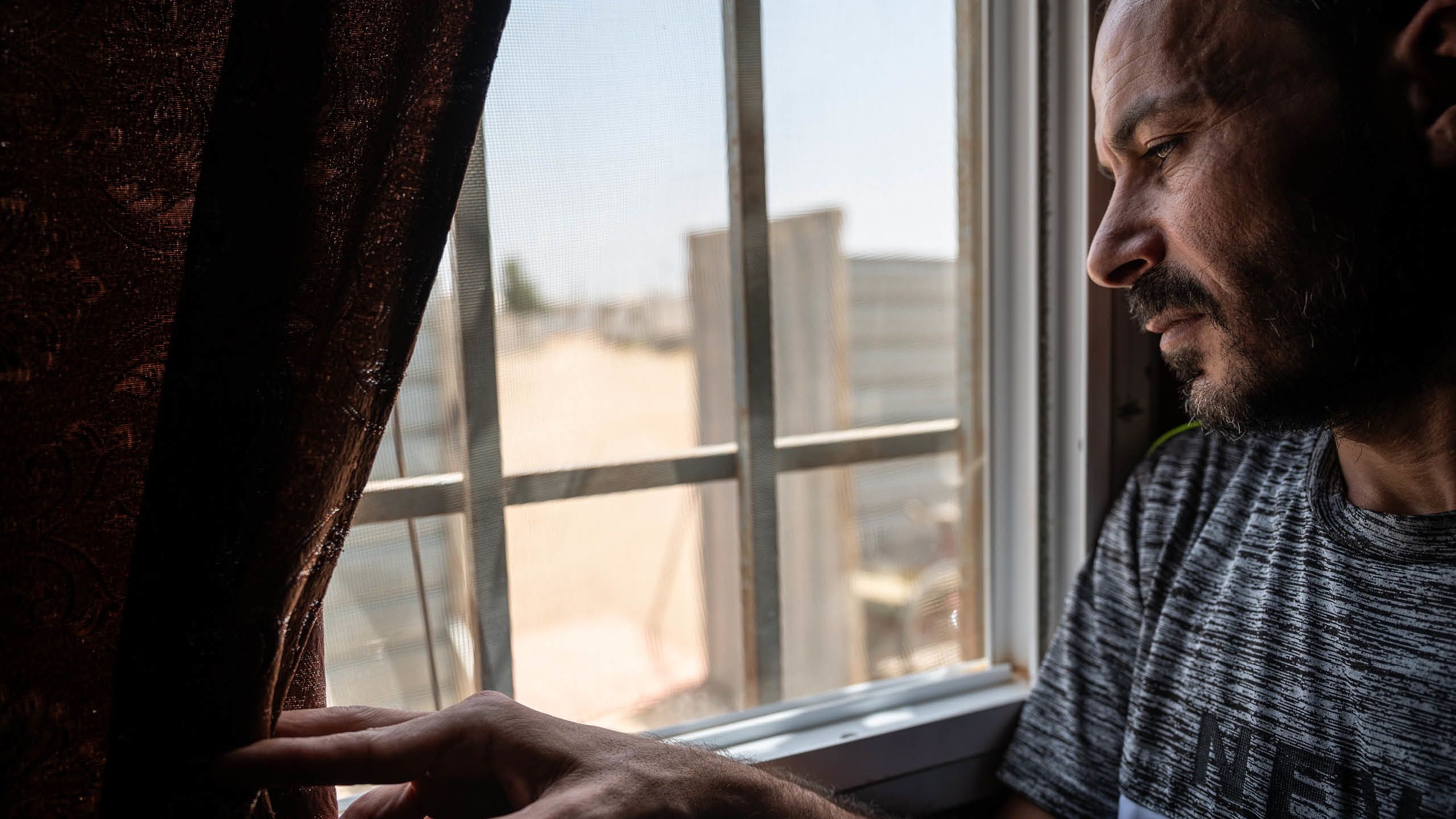 Ashraf skyver gardinen til siden og ser ut av vinduet.