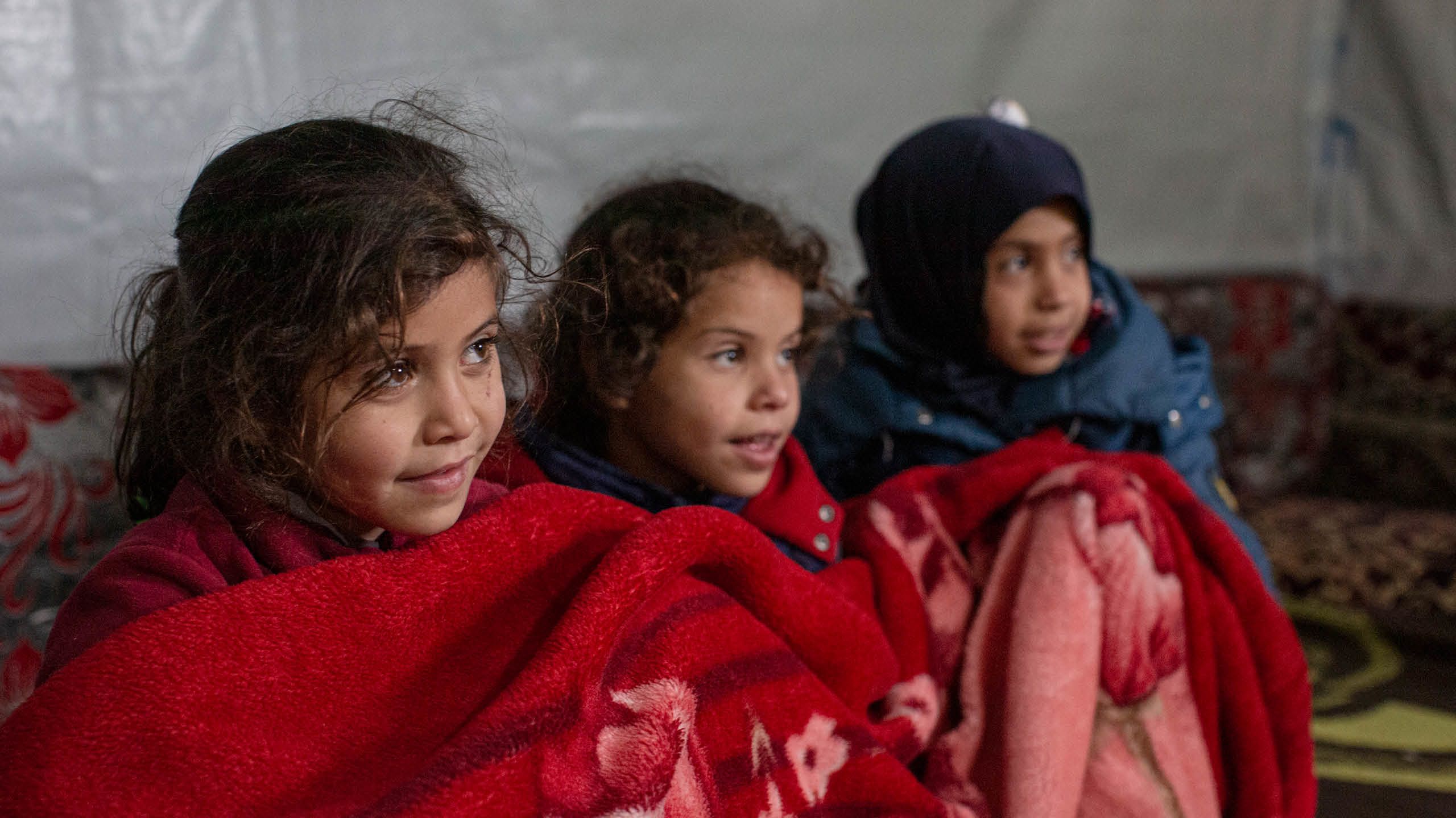 Amira (8), Aya (6) og Malak Awad (10) sitter under et rødt teppe i teltet de bor i.