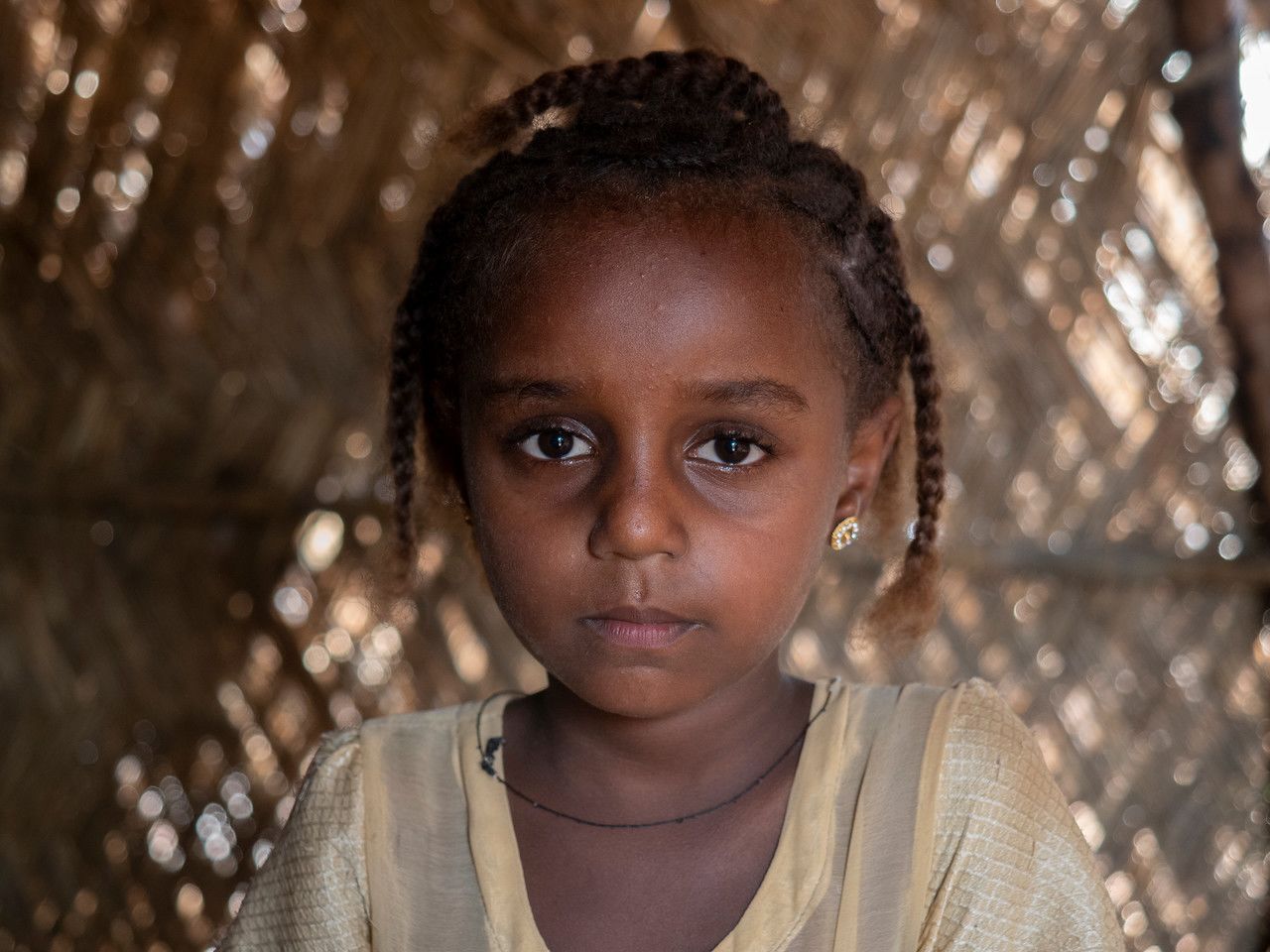 Portrait of Melat, a young girl from Ethiopia. She has braids in her hair and is wearing a light yellow top.
