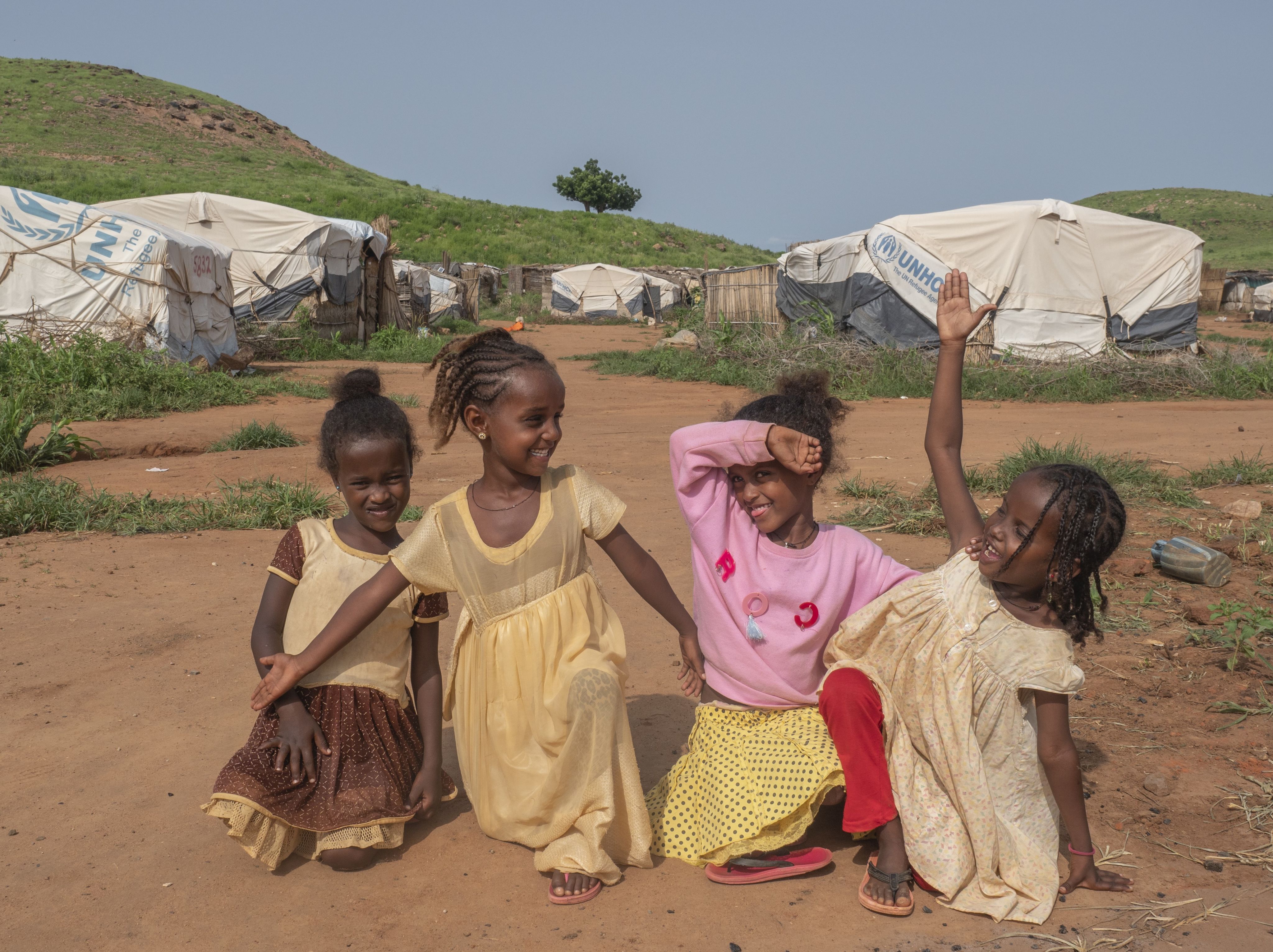 Four young girls sit together on the ground and play.