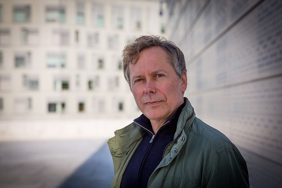 Portrait of professor Jon-Håkon Schultz, a man with greying hair and a green jacket. He is standing in front a tall building.