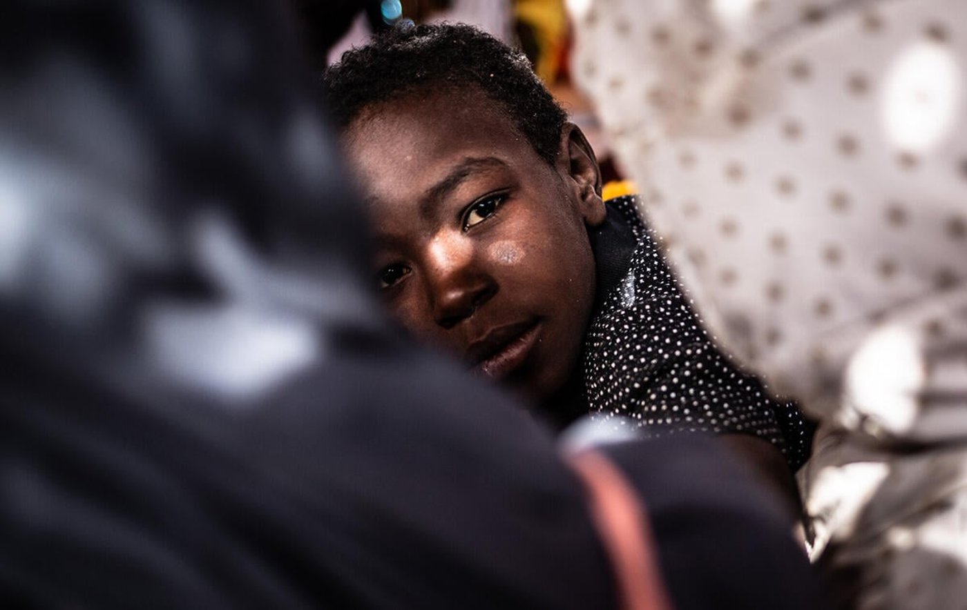 En ungdom ser på fotografen gjennom to av sine medelever. De sitter i et klasserom.