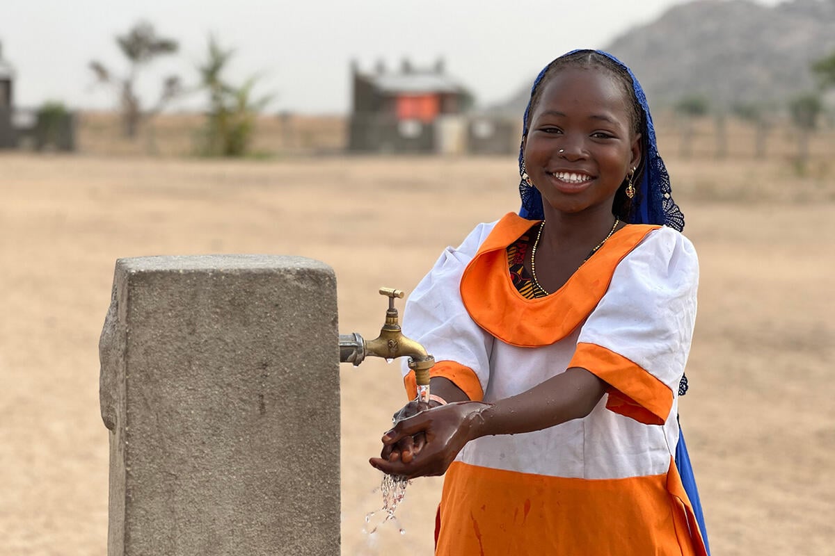 En ung jente vasker hendene sine i en kran i skolegården.